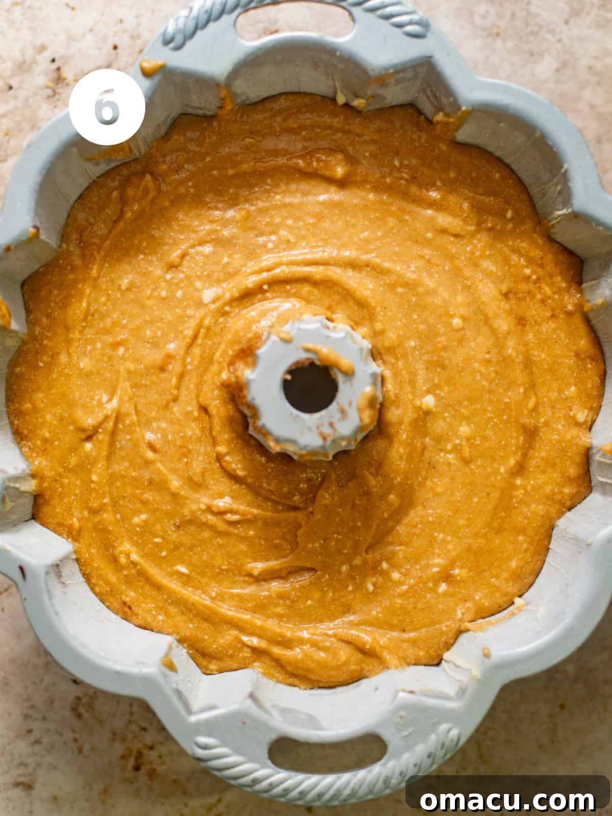 A bundt pan filled with layered sweet potato pound cake batter, showcasing the cinnamon swirl before baking.