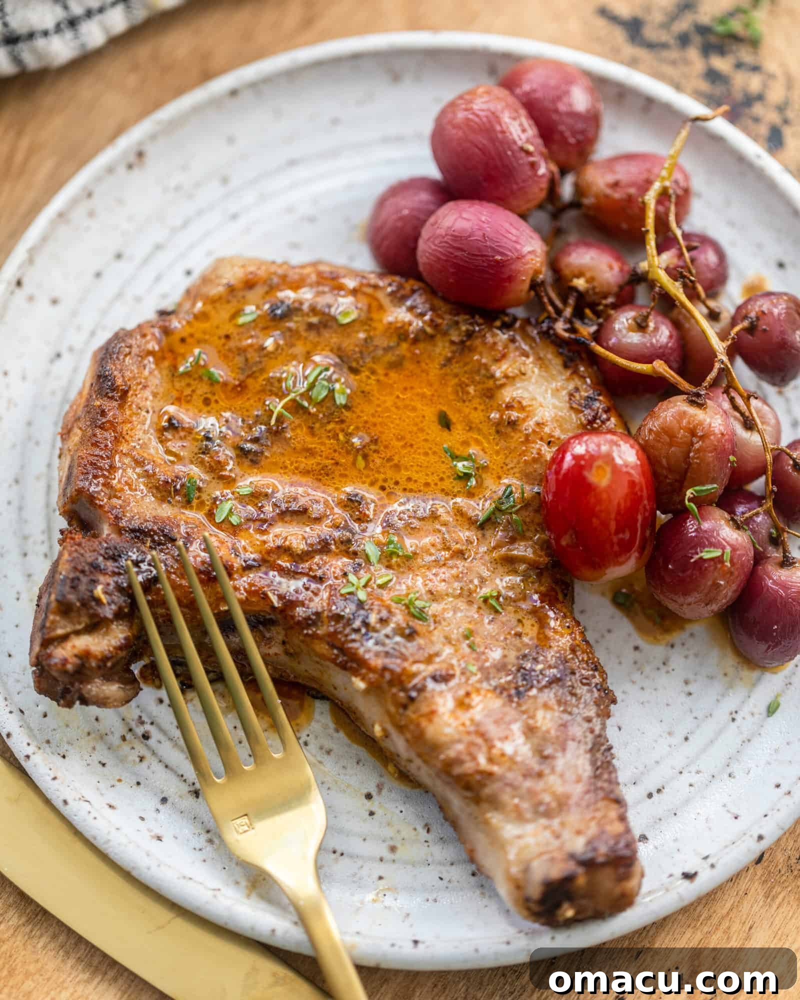 A perfectly cooked pork chop with roasted grapes on a plate, ready to be enjoyed with a fork.