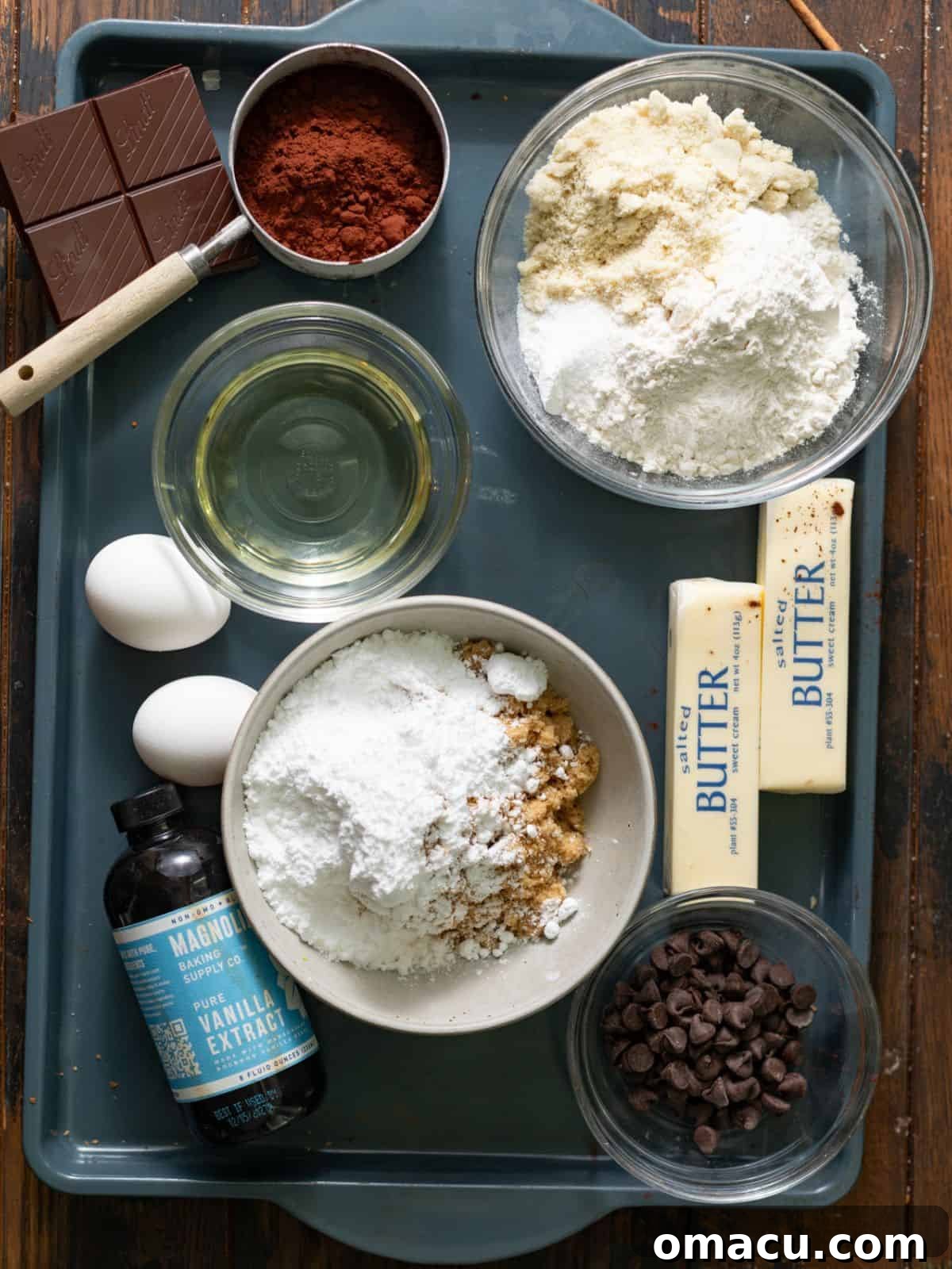 A selection of essential baking ingredients for chocolate loaf cake, including flour, cocoa powder, eggs, oil, and sour cream, neatly arranged on a baking sheet.