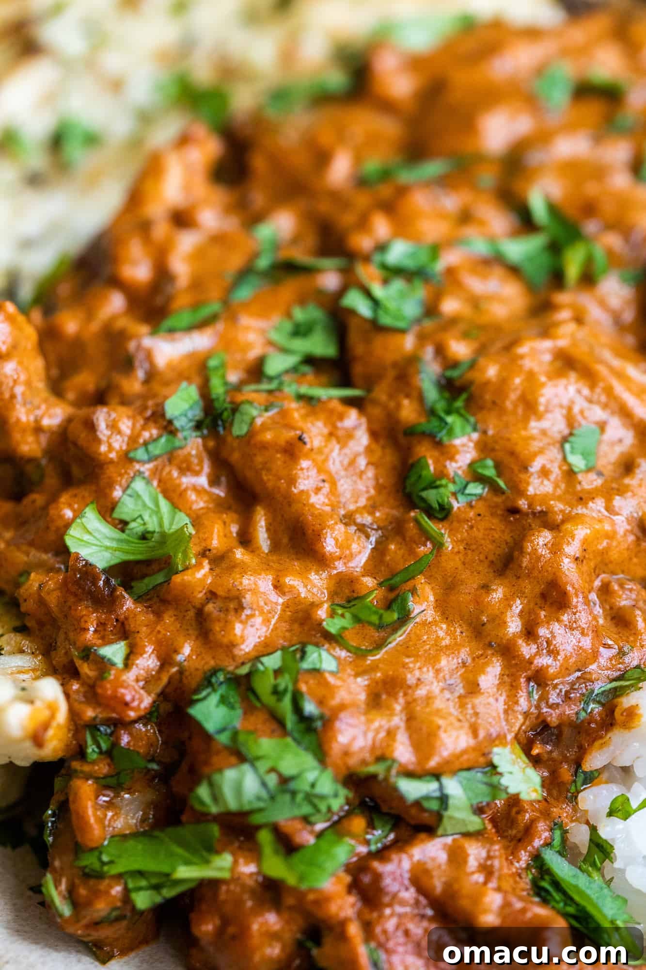 Close-up of butter chicken simmering in a cast iron skillet, garnished with fresh cilantro