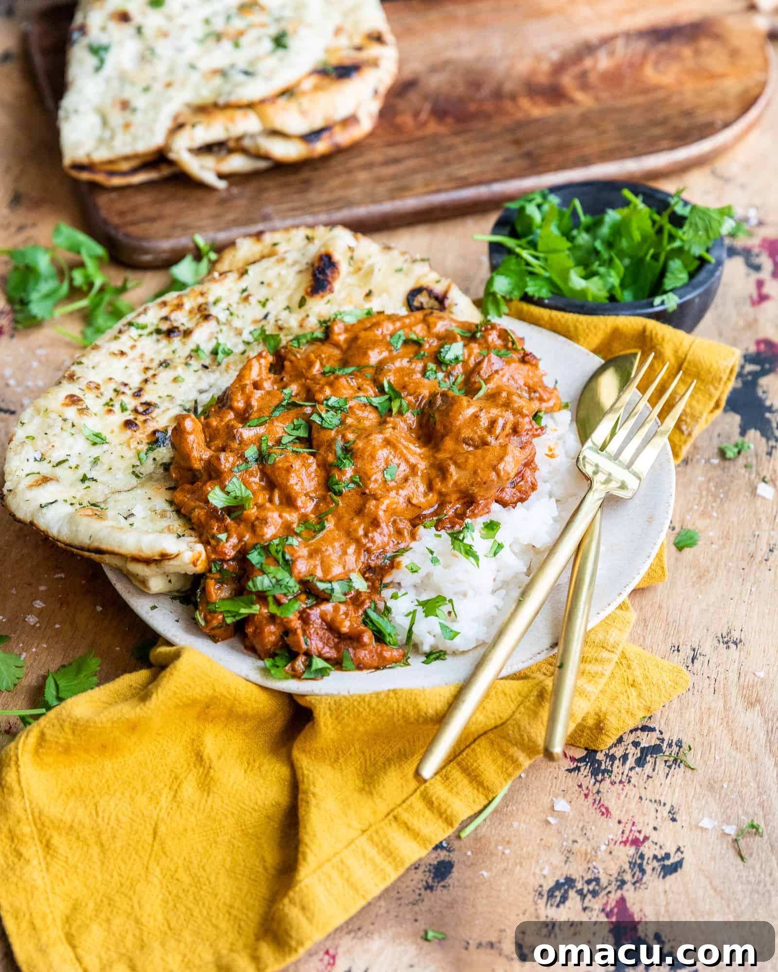 Garnished butter chicken, fresh with cilantro, served hot in a skillet with naan on the side