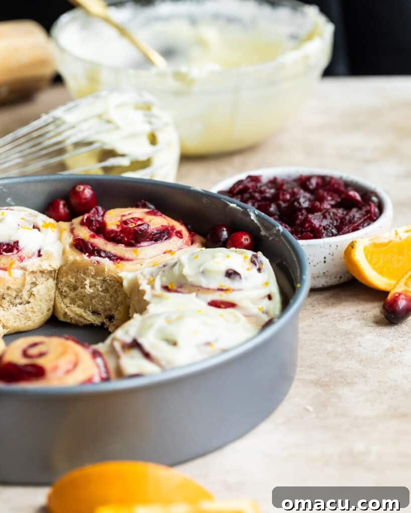 Warm cranberry cinnamon rolls with a generous drizzle of orange icing in the background, ready to be enjoyed.
