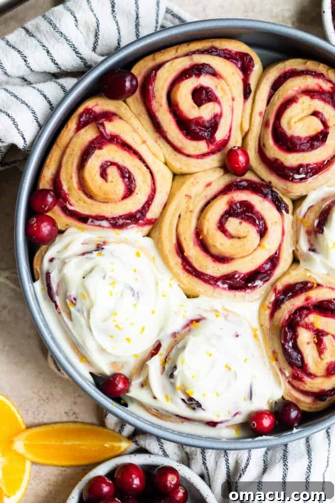 Several plump cranberry cinnamon rolls, unglazed, resting on a rustic dish towel after their second rise.