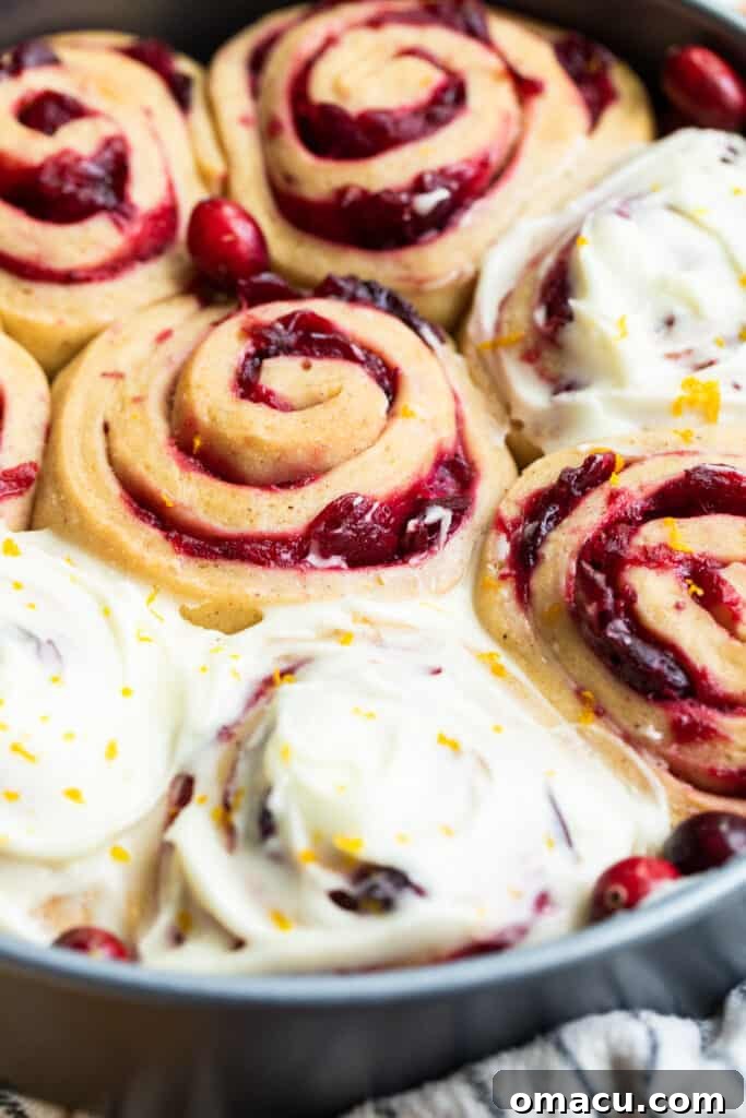A close-up of a single cranberry cinnamon roll, generously covered in creamy orange icing, emphasizing its texture.