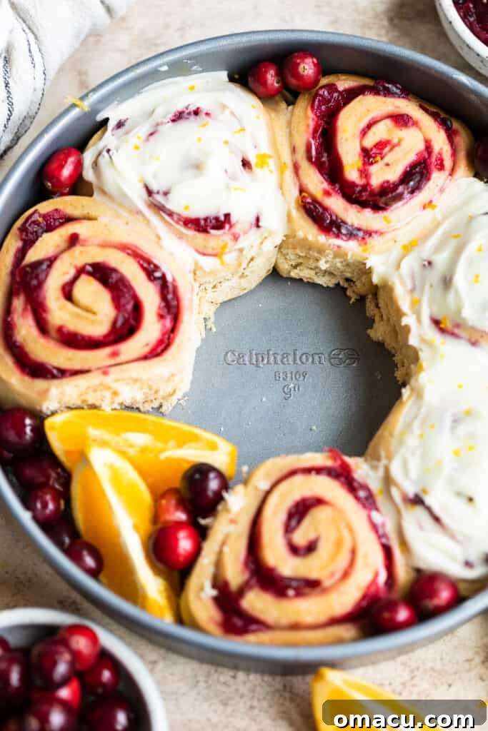 A serving of cranberry cinnamon rolls with thick, luscious orange icing drizzled generously over them, glistening and inviting.