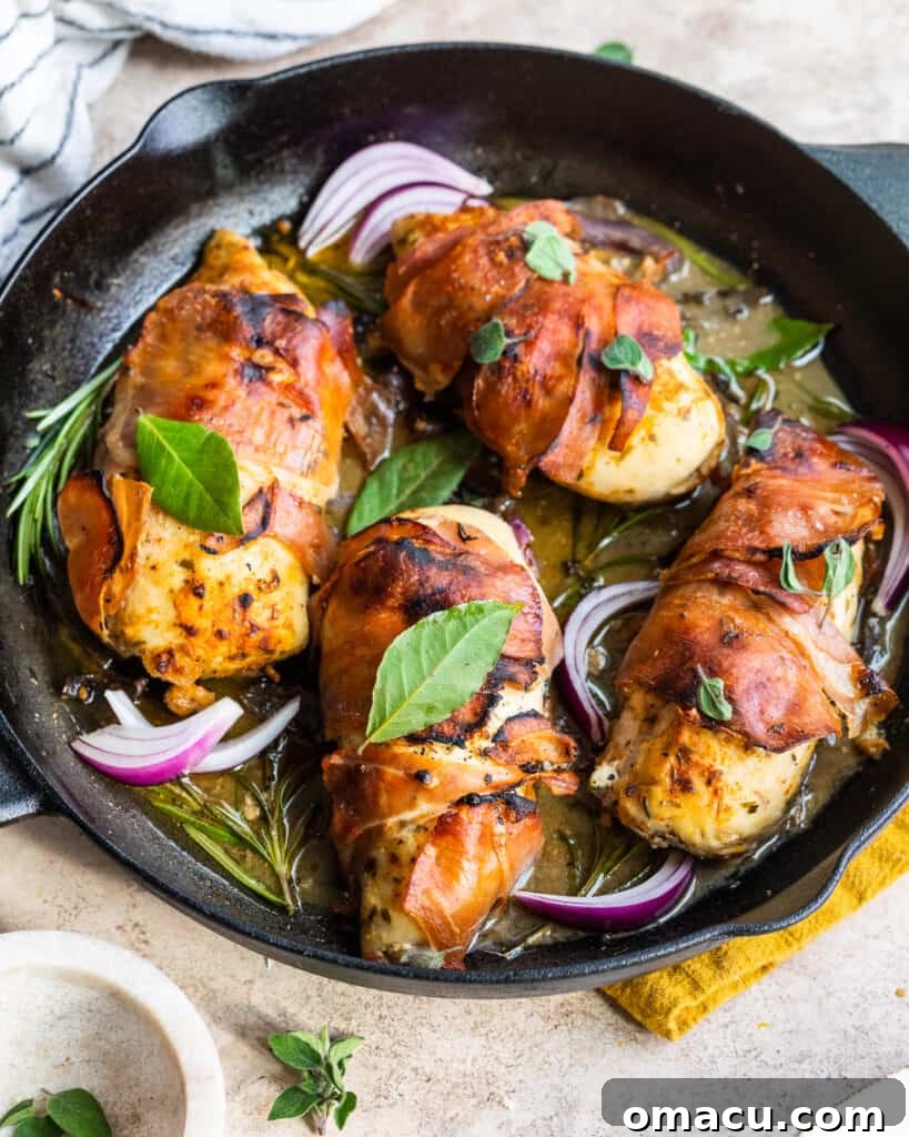 Two pieces of prosciutto wrapped chicken with fig glaze in a cast iron skillet on a striped dish cloth