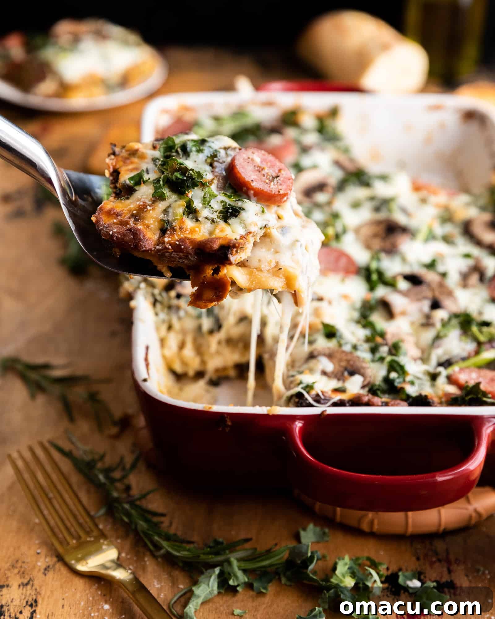 A glorious piece of Roasted Garlic Sausage Kale and Mushroom Lasagna being lifted from a baking dish, showcasing a beautiful, long cheese pull.