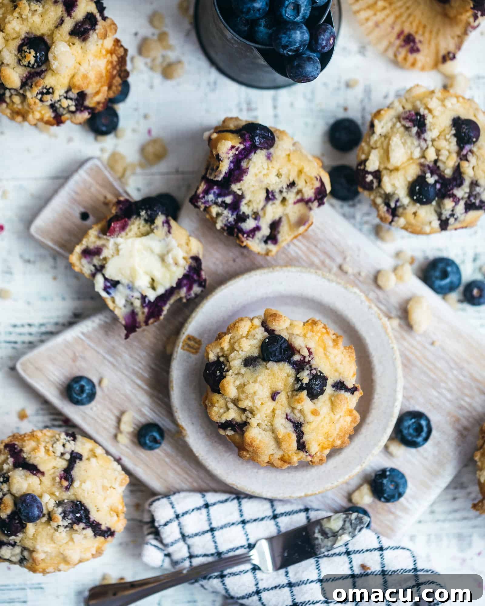 Rustic scene with blueberry muffins on a wooden cutting board, alongside a patterned dishcloth and fresh blueberries