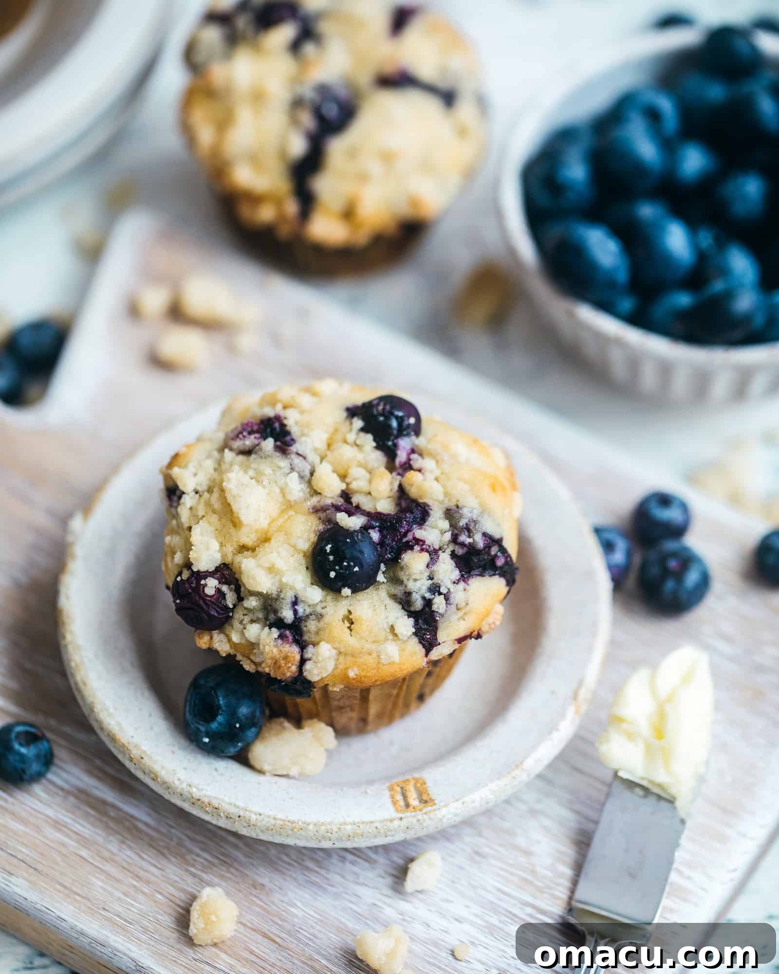 A plate of blueberry crumb cake muffins, artfully arranged with a bowl of fresh blueberries for garnish