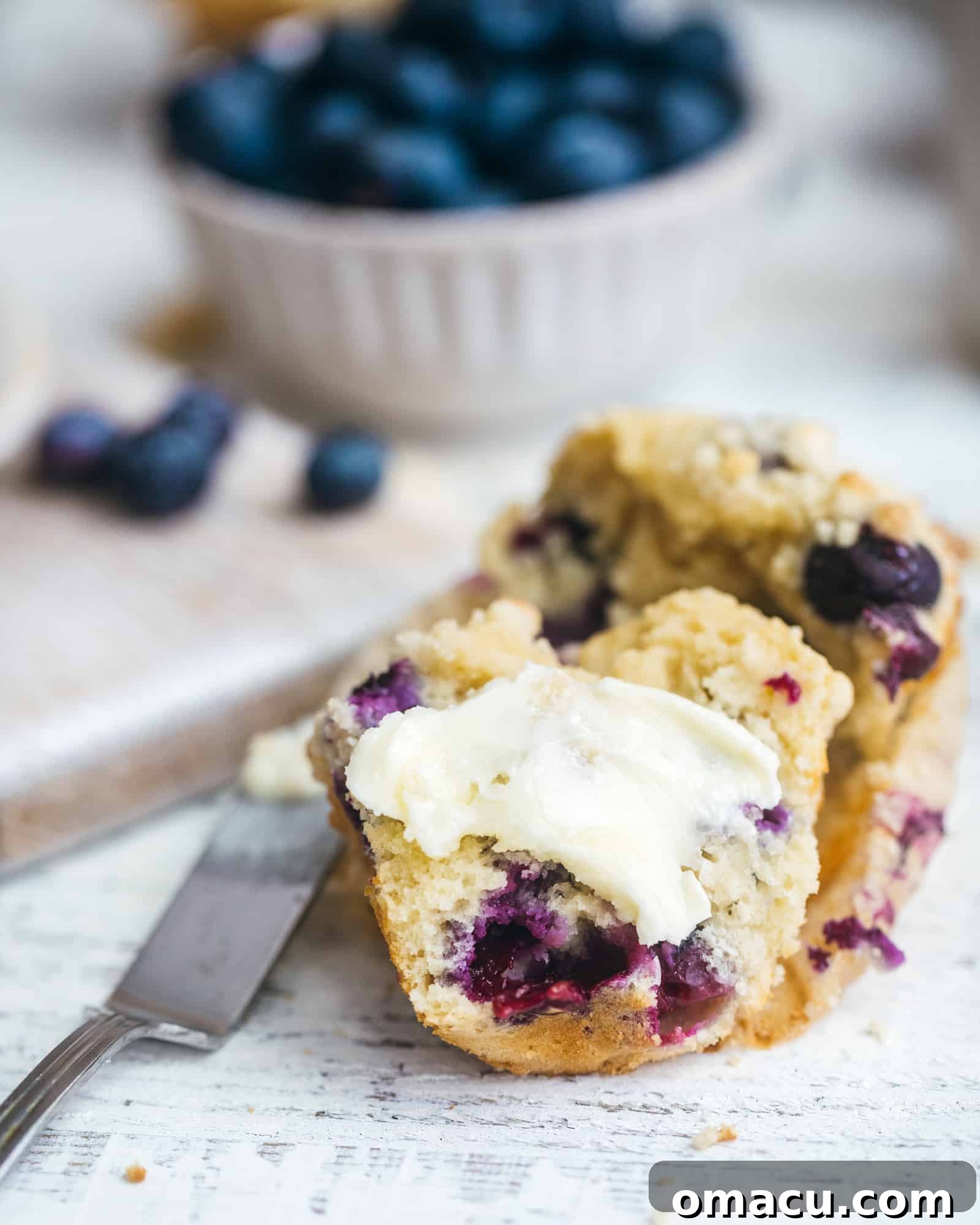 A blueberry muffin sliced in half, showcasing its rich, buttery interior, perfect for spreading with butter