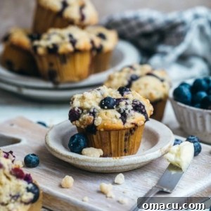 Final plated image of a blueberry crumb cake muffin on a cutting board, with a buttered knife