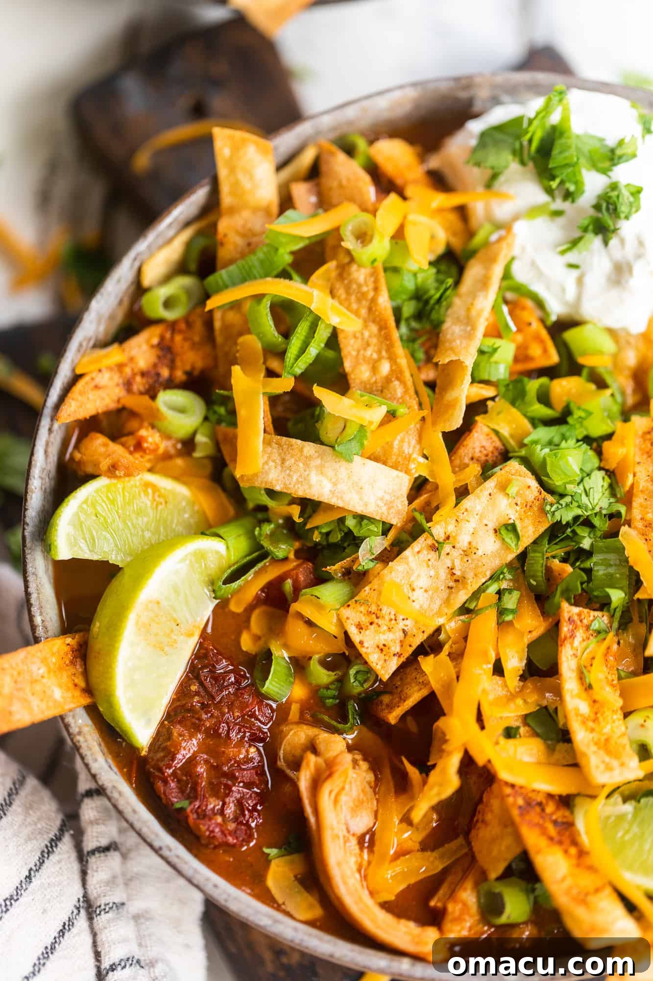 chicken tortilla soup in a bowl with sliced limes, sour cream, cilantro, and green onions on top