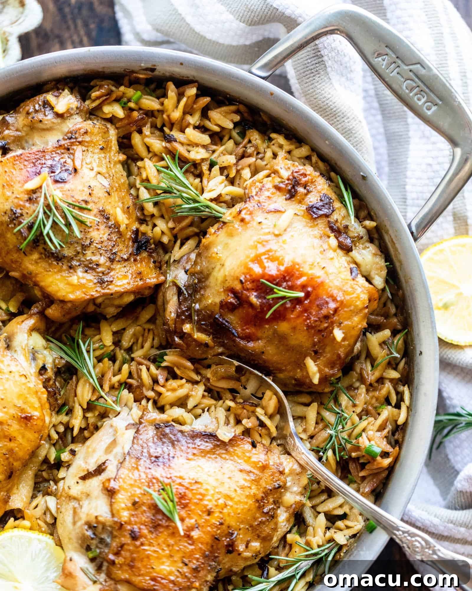 rosemary chicken with parmesan orzo in a pan with a spoon and lemons