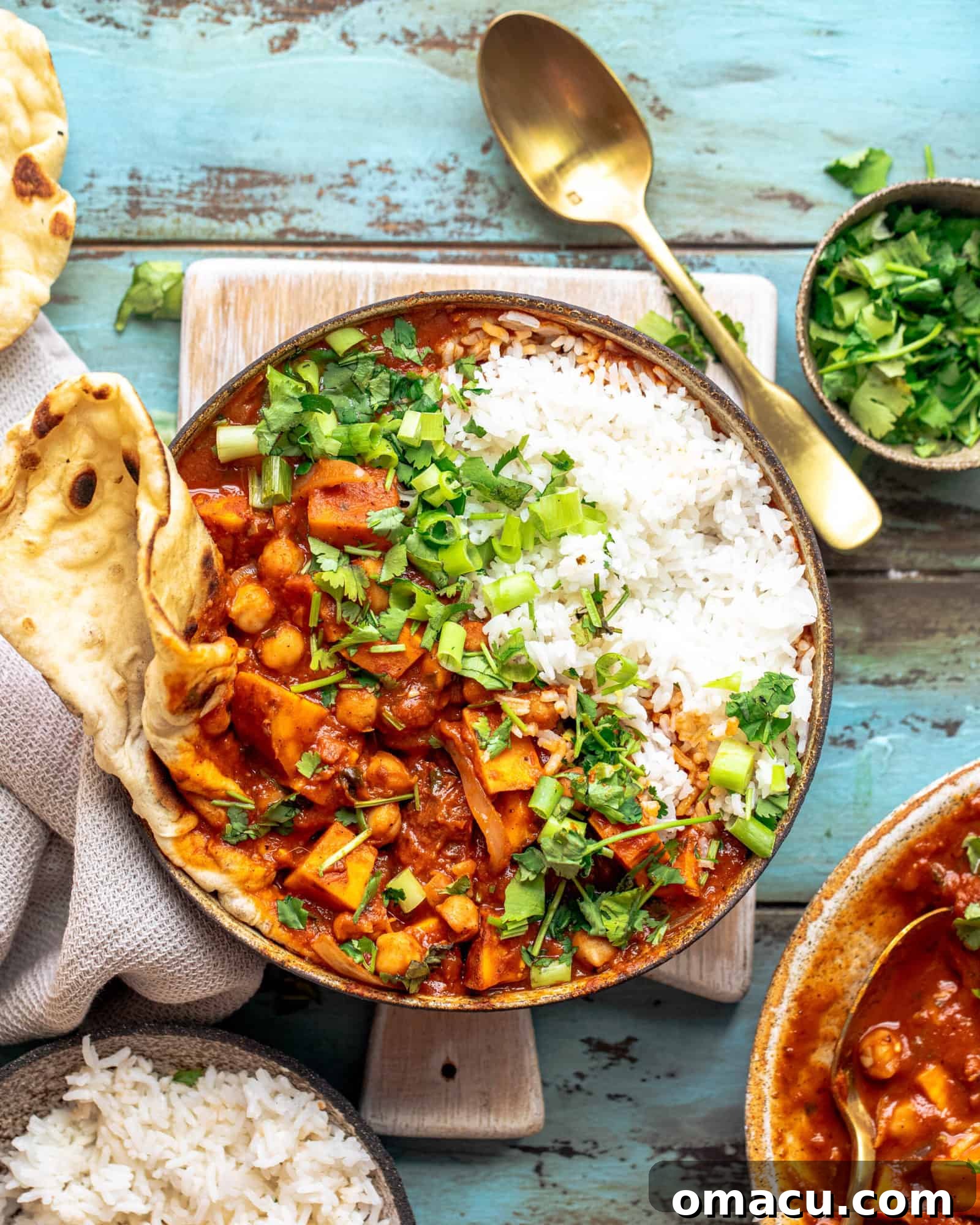 A vibrant bowl of Sweet Potato Chickpea Curry with fresh cilantro, ready to be enjoyed, resting on a rustic cutting board. Steam rises invitingly from the dish.