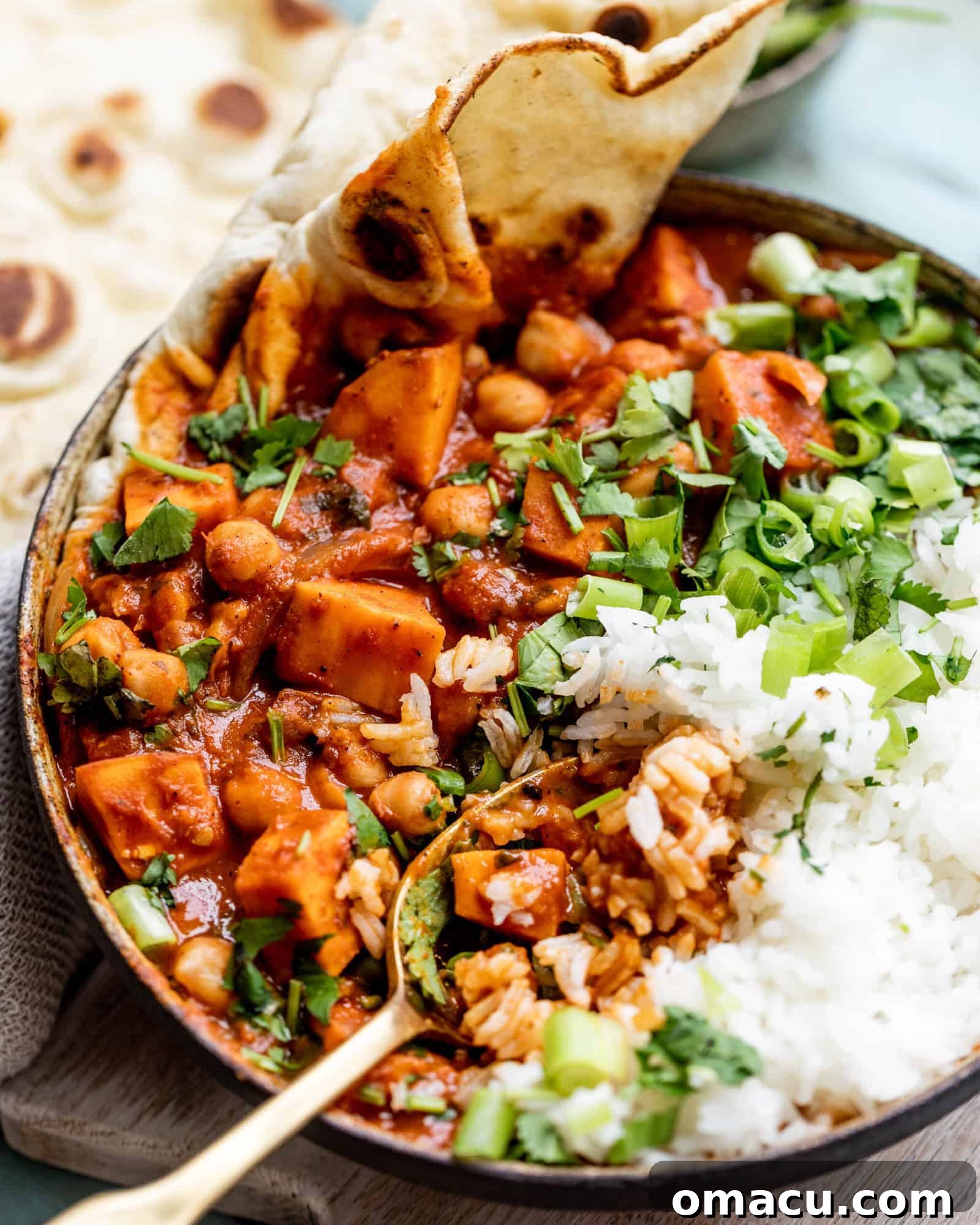 Close-up shot of creamy Sweet Potato Chickpea Curry in a bowl with a spoon, showing its rich texture, chunks of sweet potato, and colorful ingredients.
