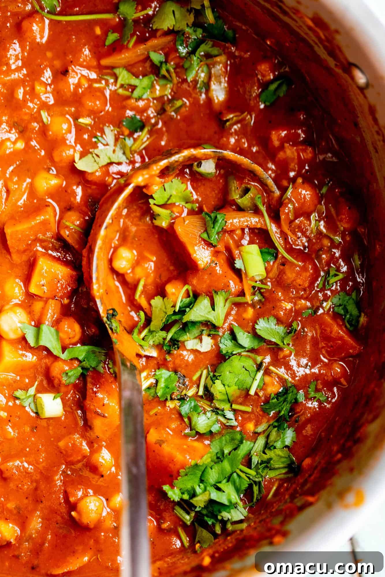 Sweet Potato Chickpea Curry simmering in a large pot with a ladle resting inside, showcasing its rich, thick texture and vibrant colors before serving.