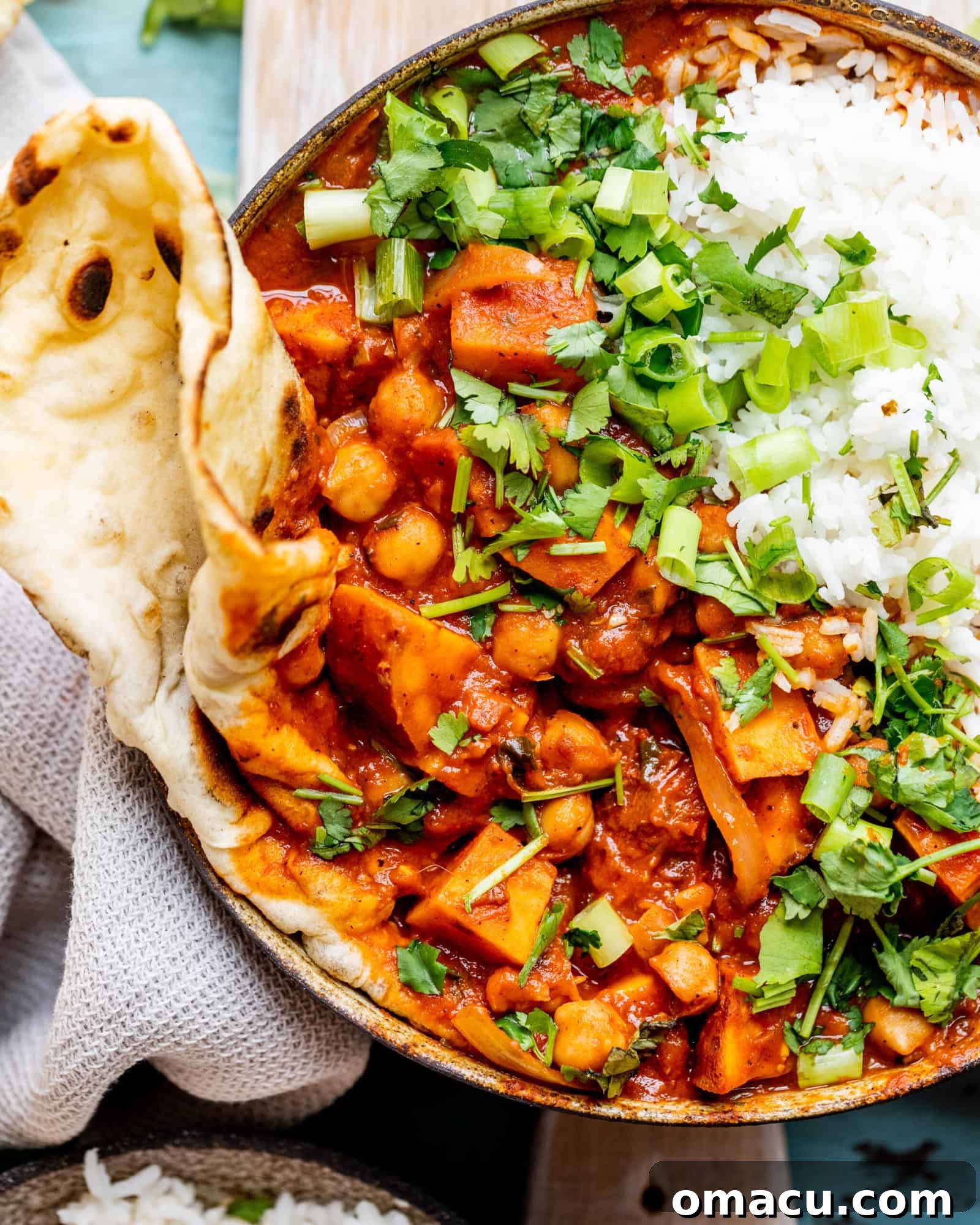 A generous serving of Sweet Potato Chickpea Curry in a bowl, accompanied by fluffy garlic naan bread, placed on a dark table, ready to be dipped and enjoyed.