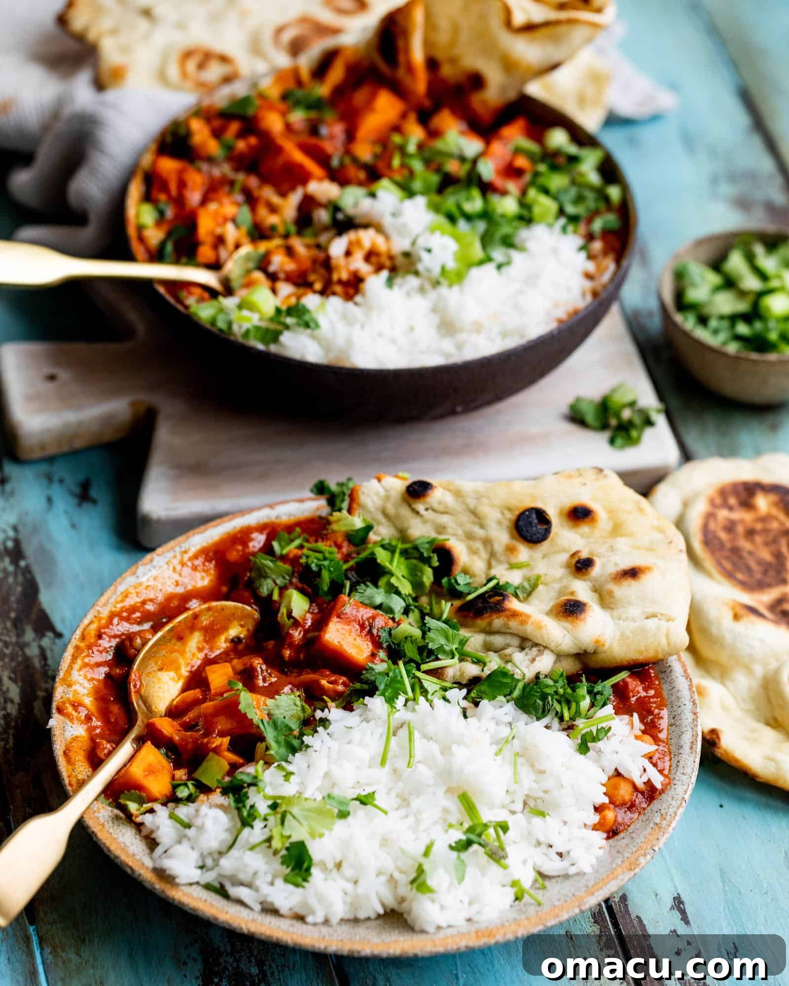 Two bowls of Sweet Potato Chickpea Curry, generously garnished with fresh herbs, served alongside fluffy white rice and warm naan bread, creating a complete and inviting meal.
