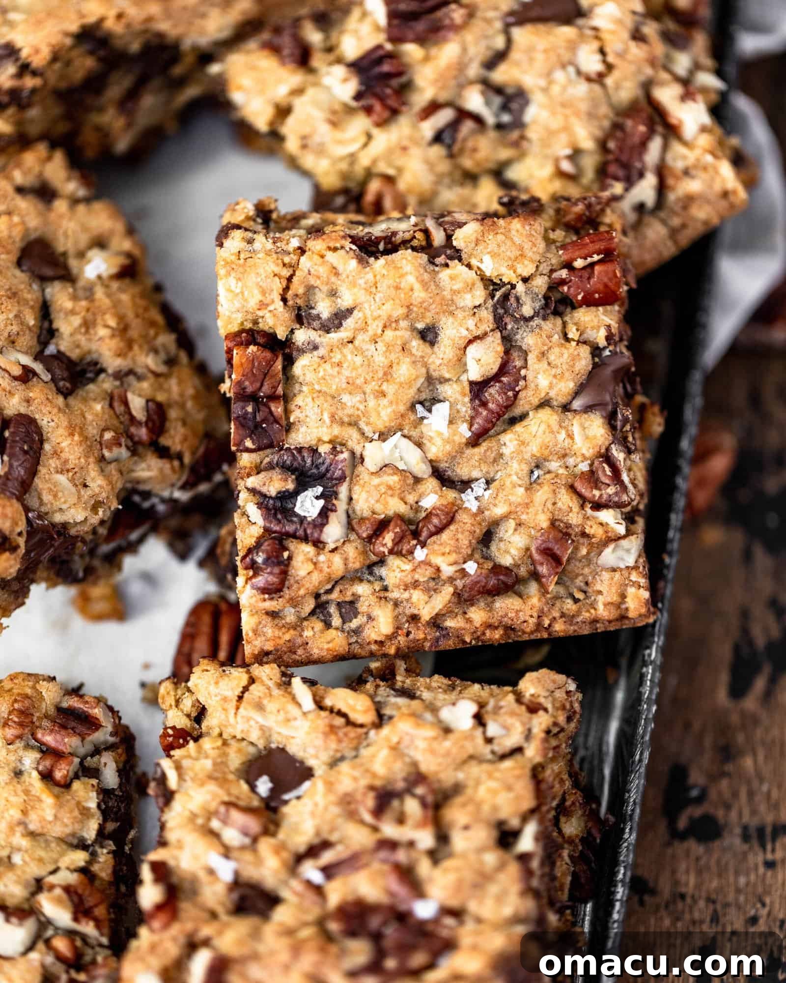 Close-up of a chocolate chip pecan oatmeal bar with flake salt on top, showing its chewy texture and melted chocolate.