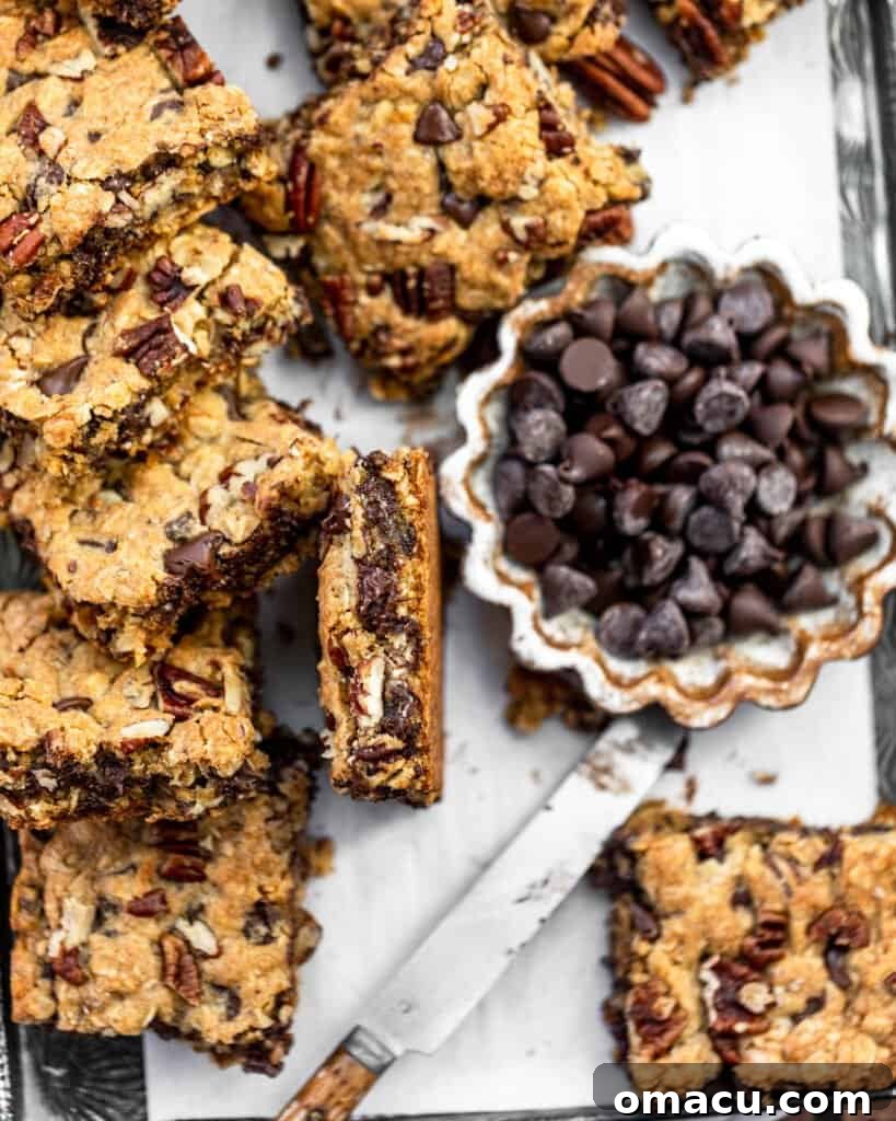 Cut chocolate chip pecan oatmeal bars arranged on a baking sheet, with a bowl of chocolate chips in the background.