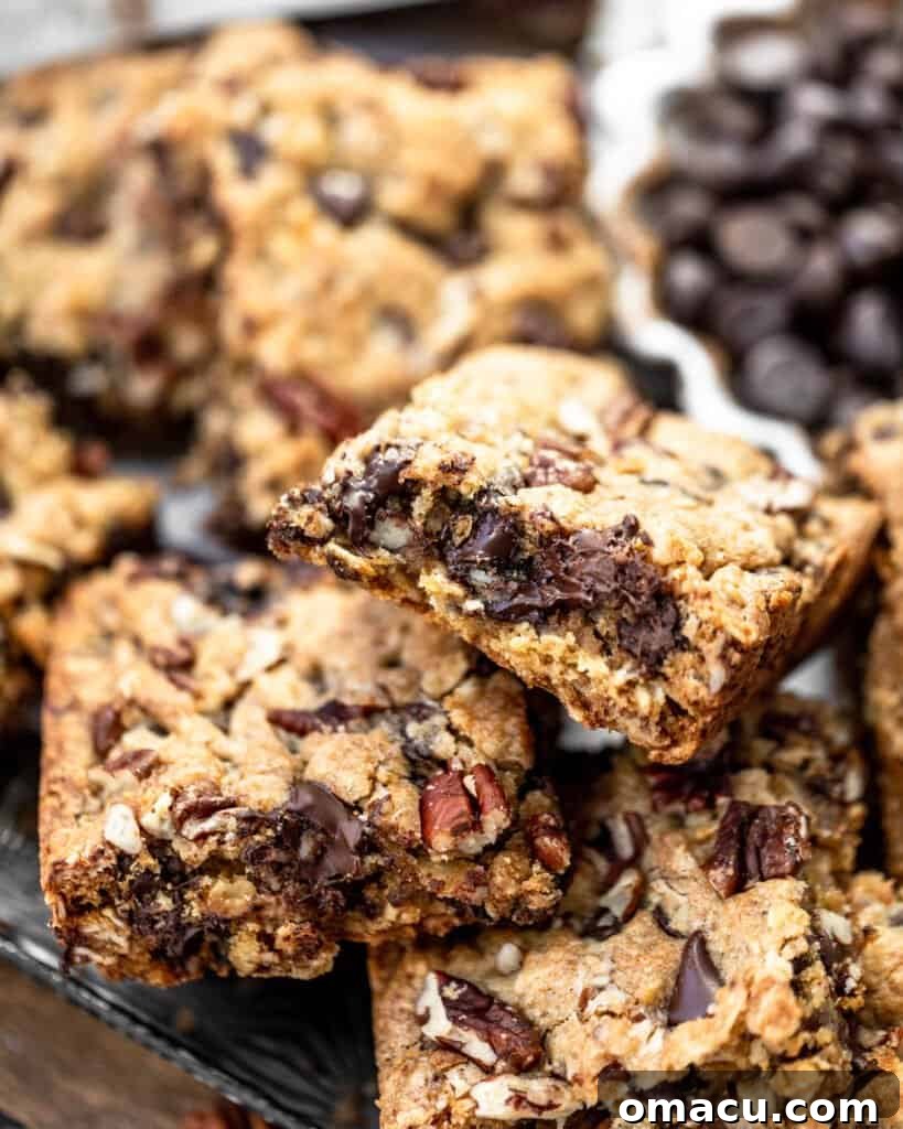Close-up of a warm chocolate chip pecan oatmeal bar, with melted chocolate oozing out, showing its delicious gooey center.