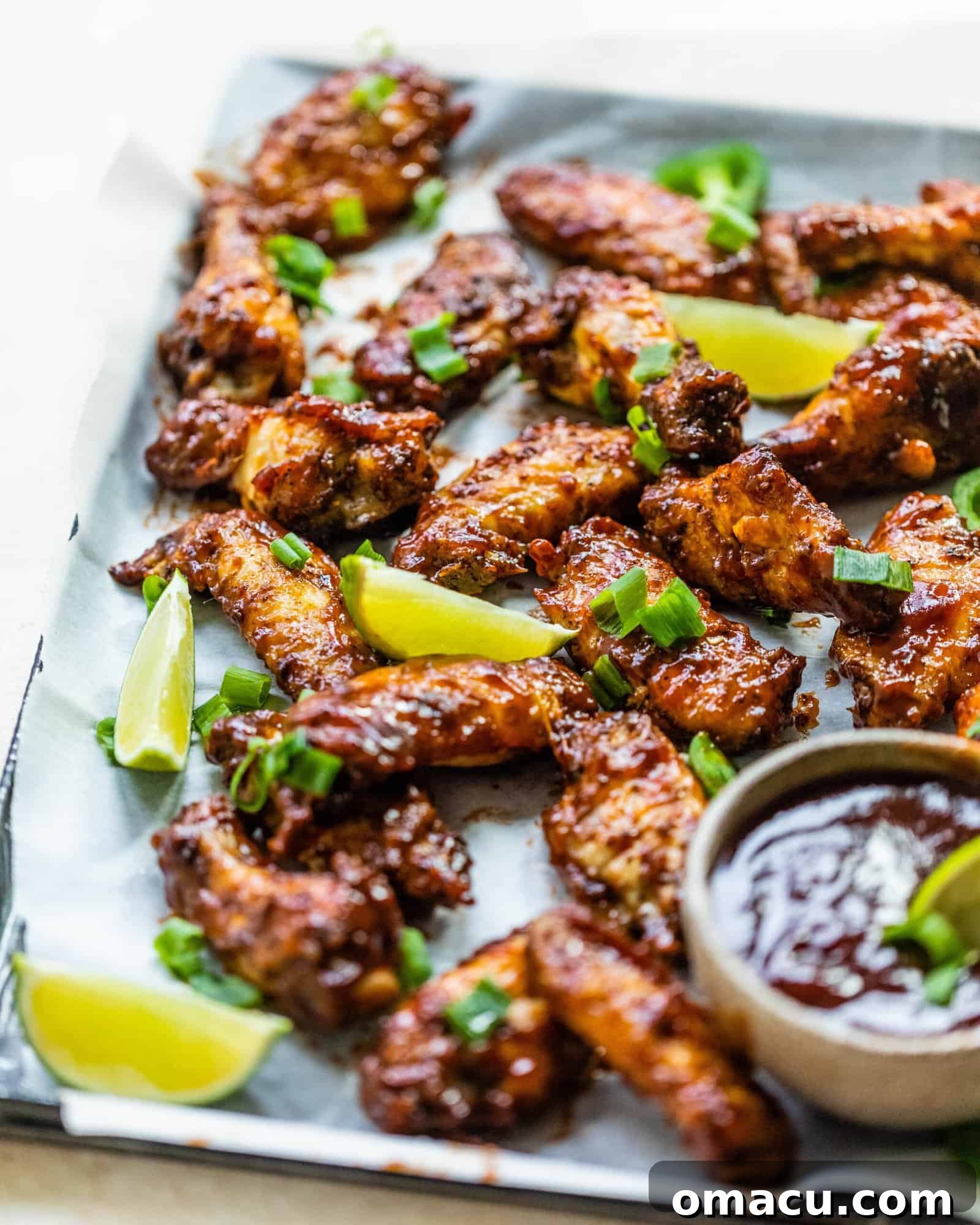 A platter of golden-brown Cajun BBQ wings, generously coated in sauce, with fresh lime wedges on the side.