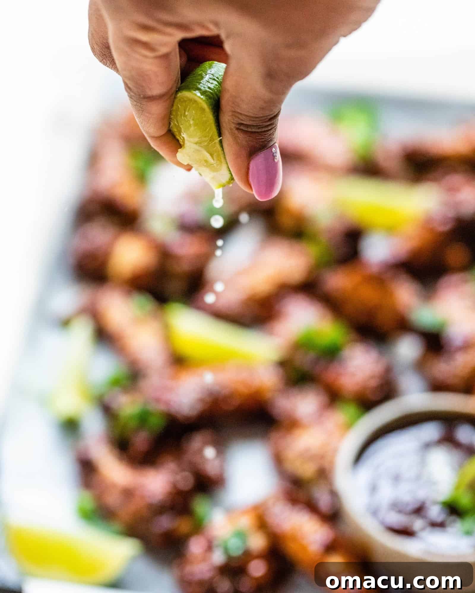 A hand squeezing a fresh lime wedge over a platter of Cajun BBQ wings, adding a burst of citrus flavor.