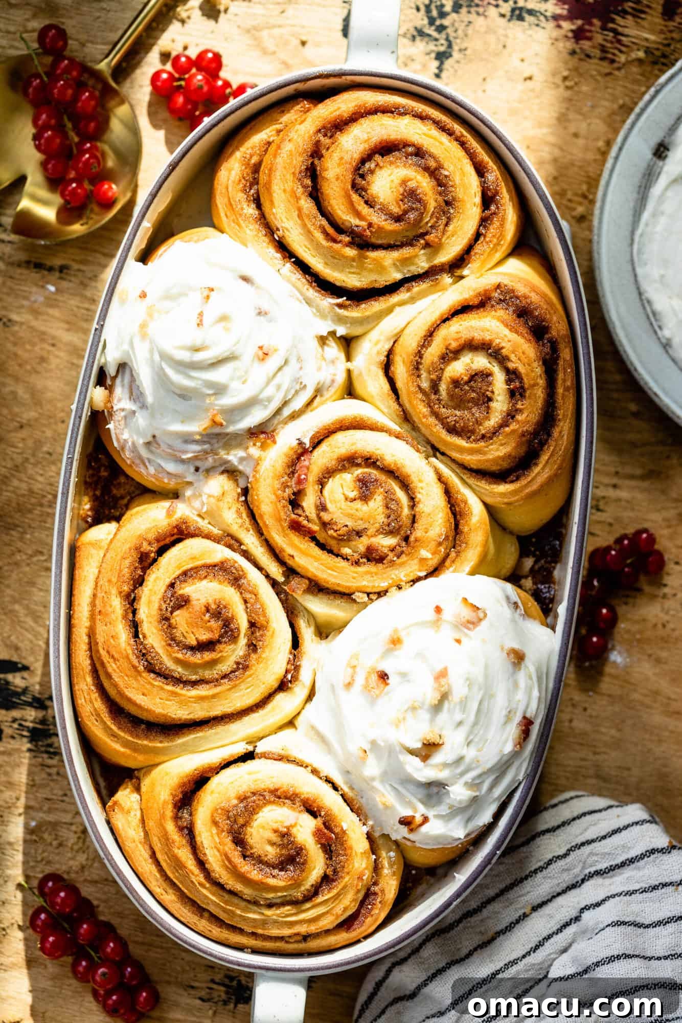 Freshly baked cinnamon rolls in a glass baking dish, topped with icing and a spoon resting nearby with a few berries.