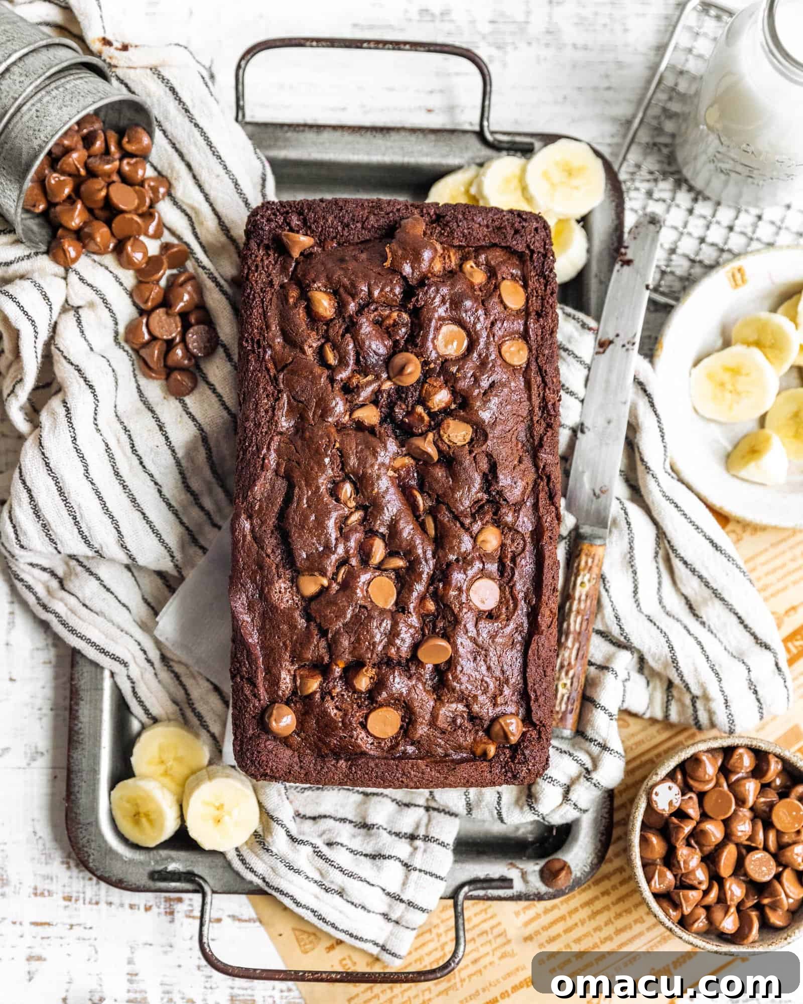 A perfectly baked loaf of chocolate banana bread on a rustic serving tray, adorned with fresh banana slices, invitingly cut into thick portions.