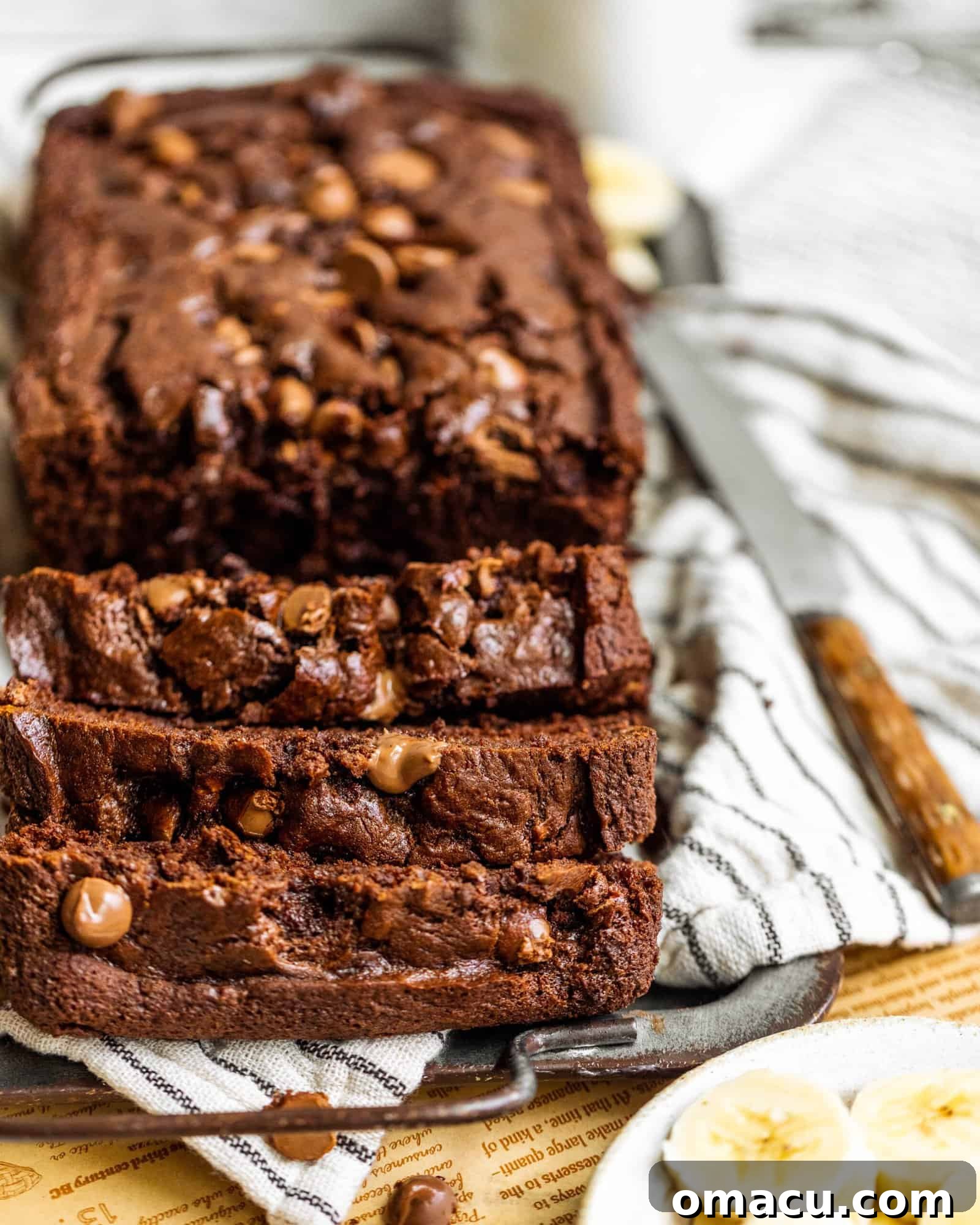A close-up shot of a thick slice of chocolate banana bread with a butter knife resting beside it, highlighting the moist interior and visible chocolate chips.