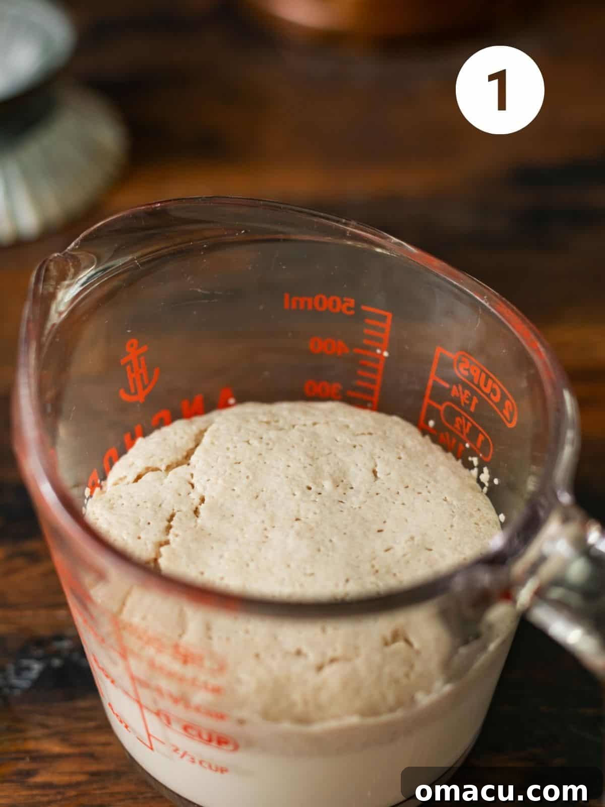 A close-up of bloomed active dry yeast, milk, and sugar mixture, showing a frothy, bubbly surface in a glass measuring cup.