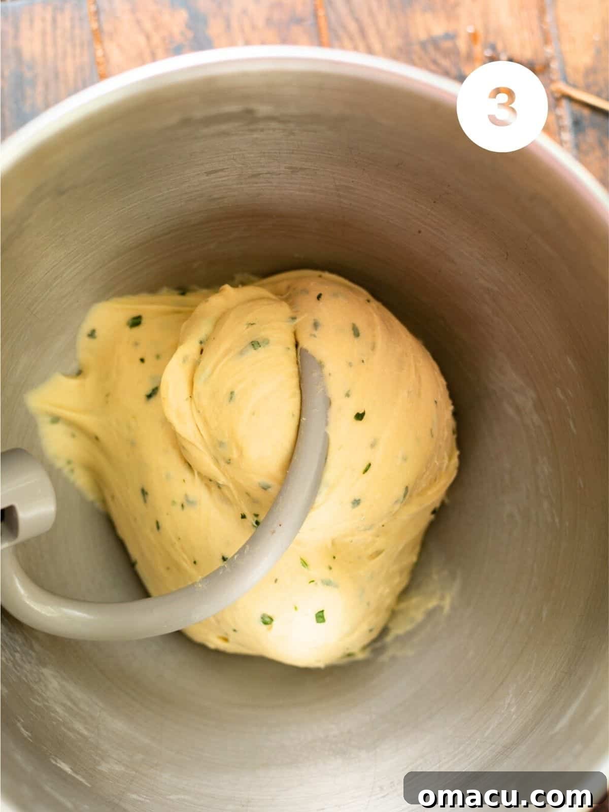 The smooth, risen garlic butter rolls dough in an oiled mixing bowl, covered with plastic wrap.