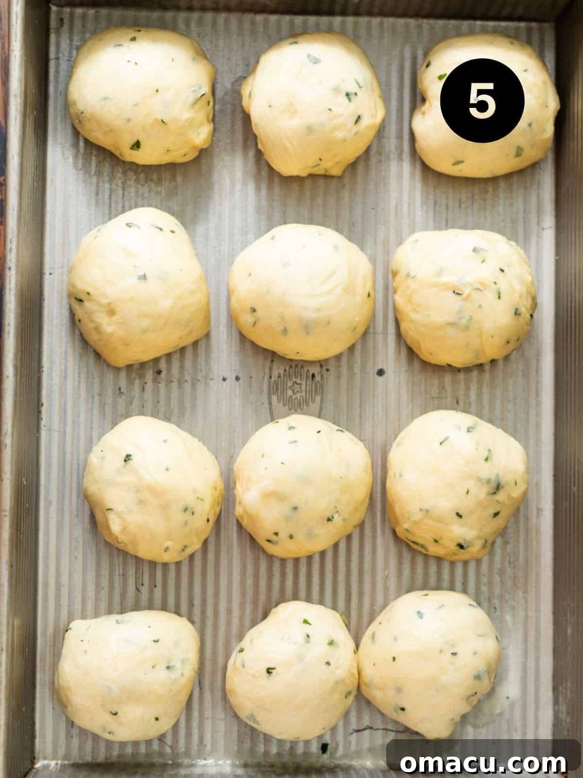 Twelve individual garlic butter rolls shaped and arranged in a 9x13 inch metal baking pan, ready for their second rise.