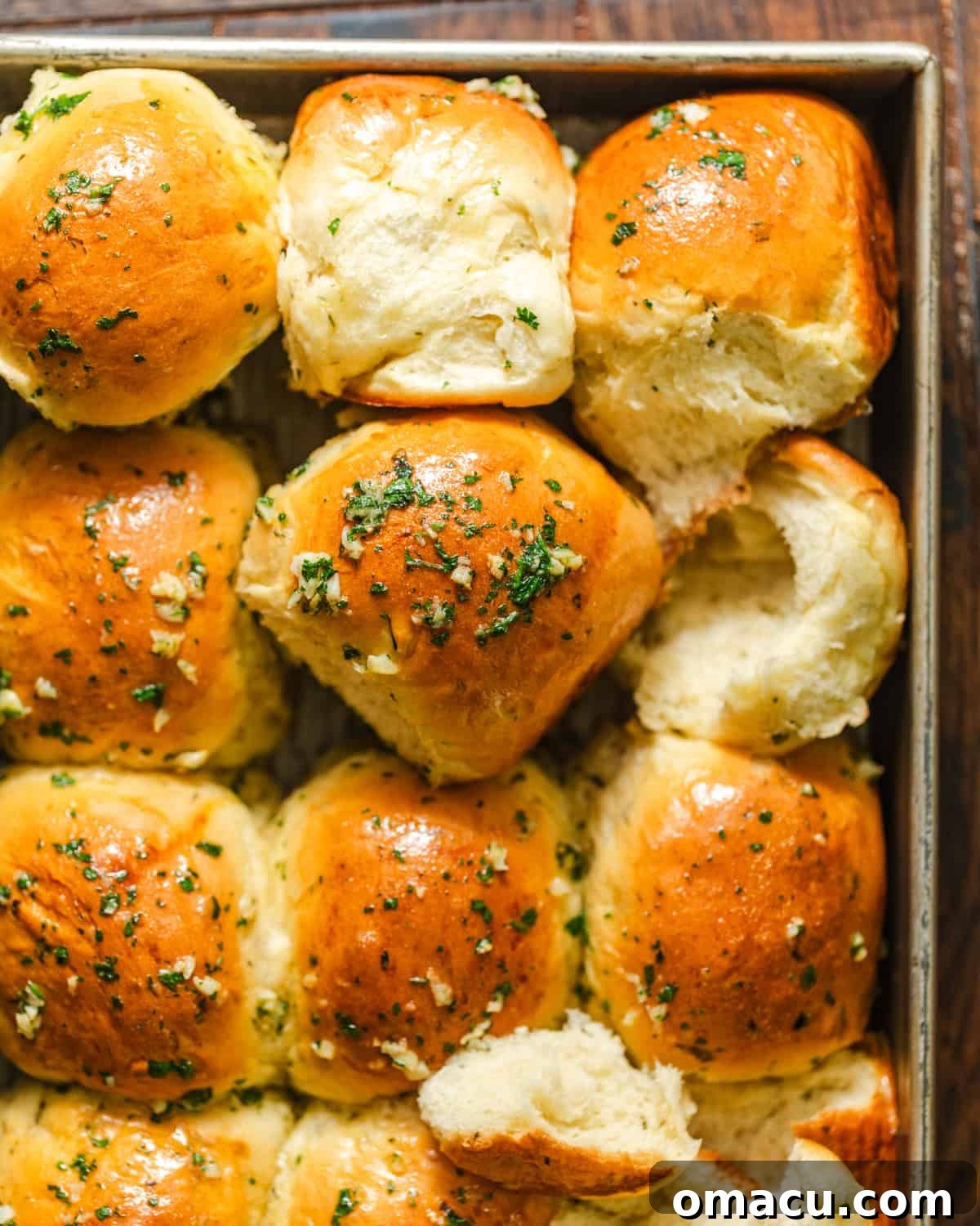 A close-up of several garlic butter dinner rolls in a pan, heavily brushed with melted garlic butter and sprinkled with flaky sea salt.