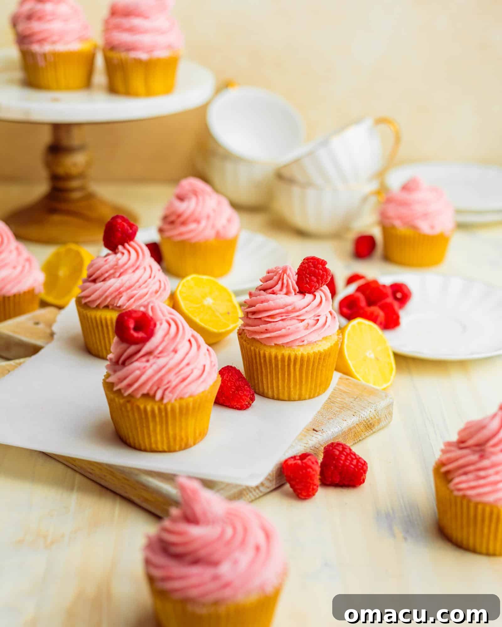 lemon raspberry cupcakes on a serving board with fresh raspberries and lemon slices
