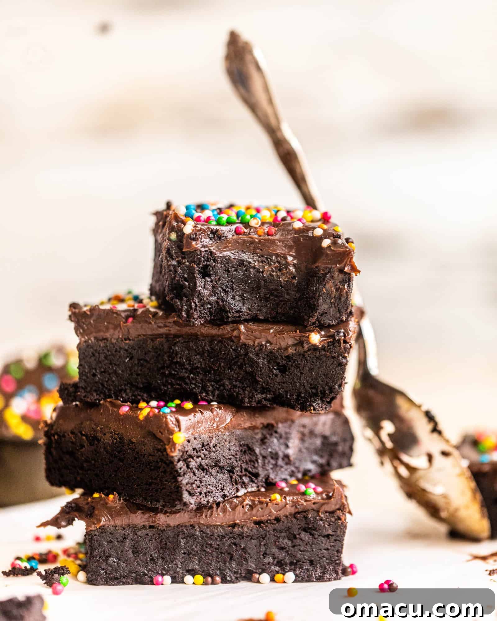 Stacked fudgy cosmic brownies with a spoon ready for a bite, showcasing their rich chocolate ganache and colorful sprinkles.