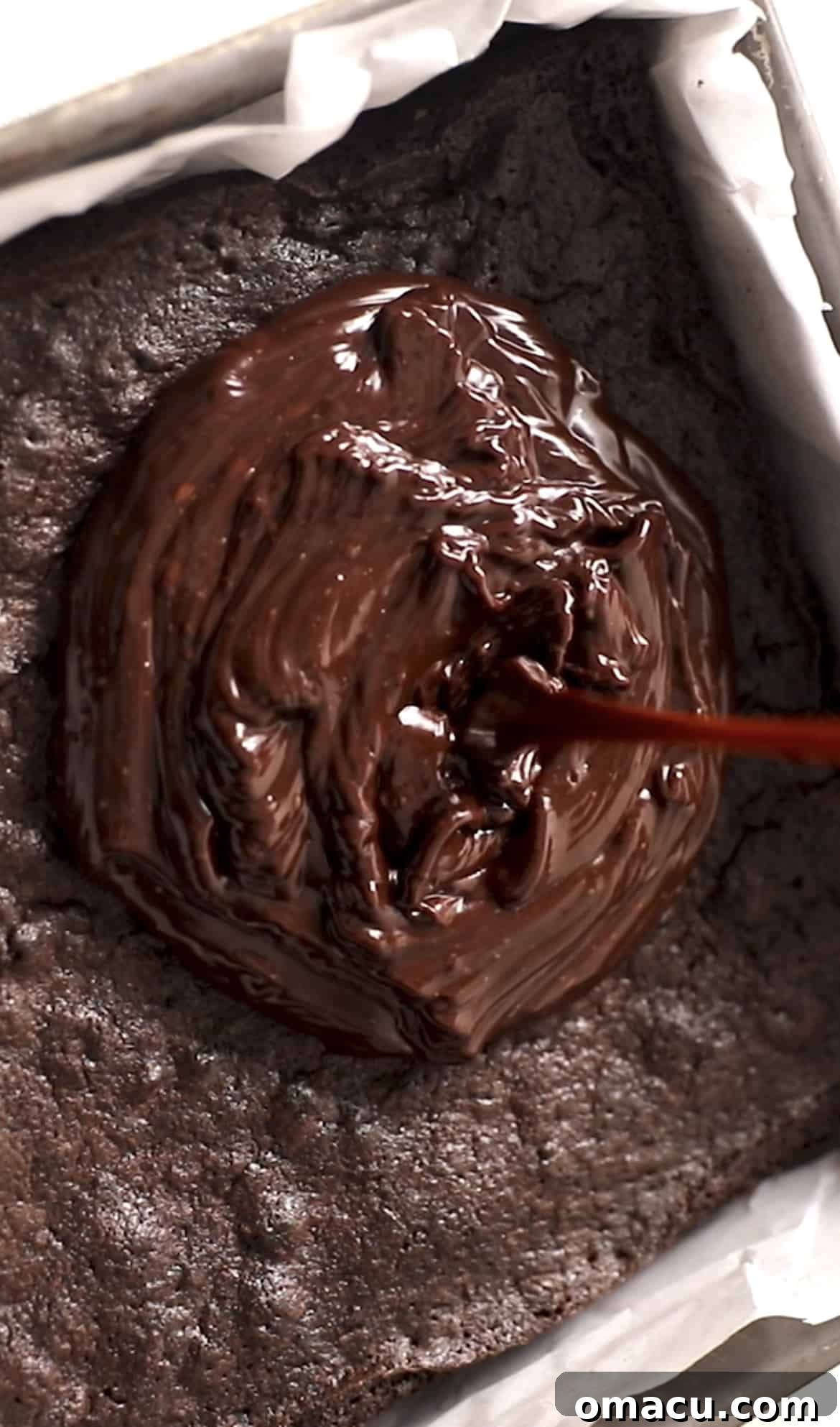 Pouring rich chocolate ganache over a tray of perfectly cooled homemade brownies.