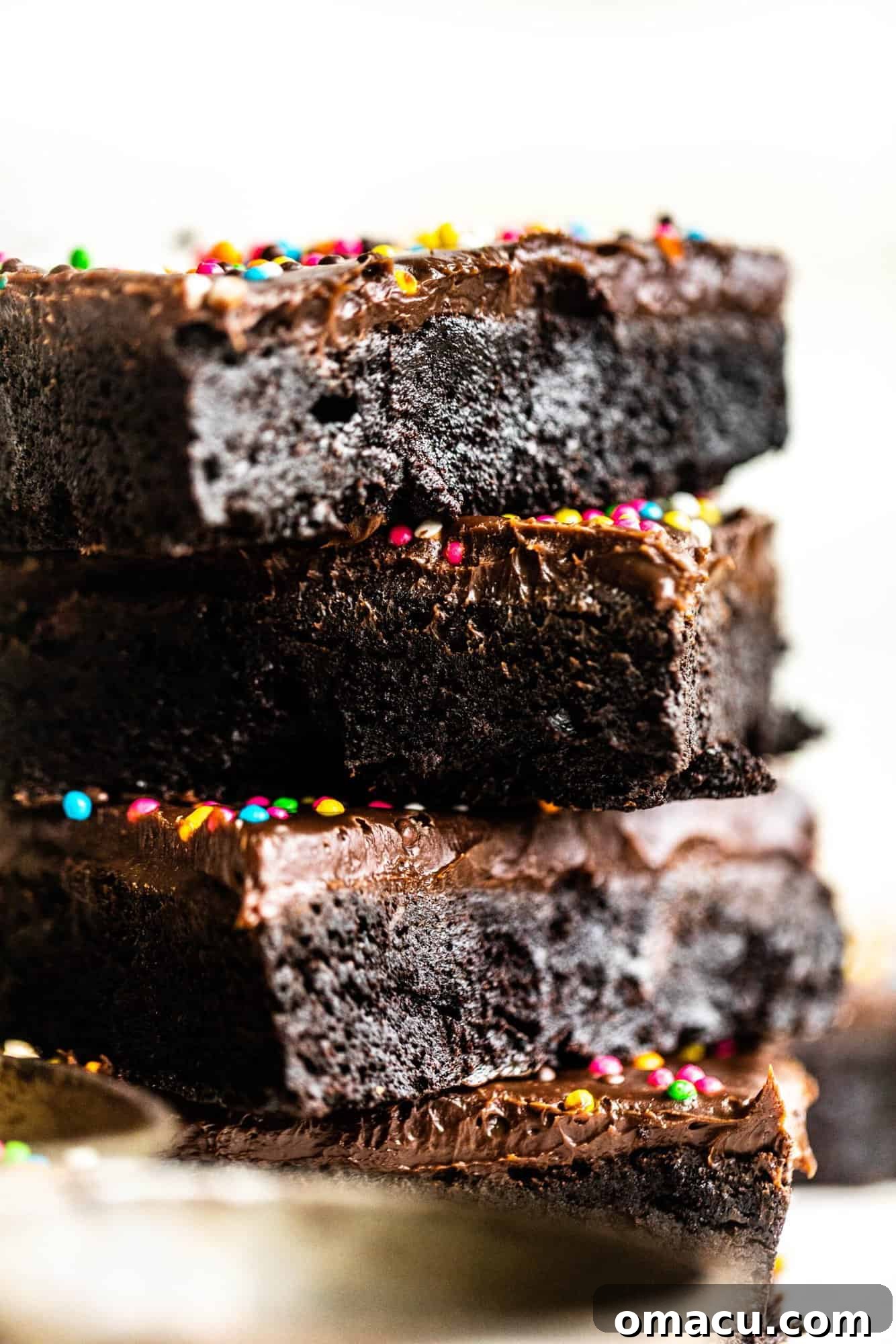 Close-up of stacked homemade cosmic brownies, highlighting the glossy ganache and vibrant rainbow crunch sprinkles.