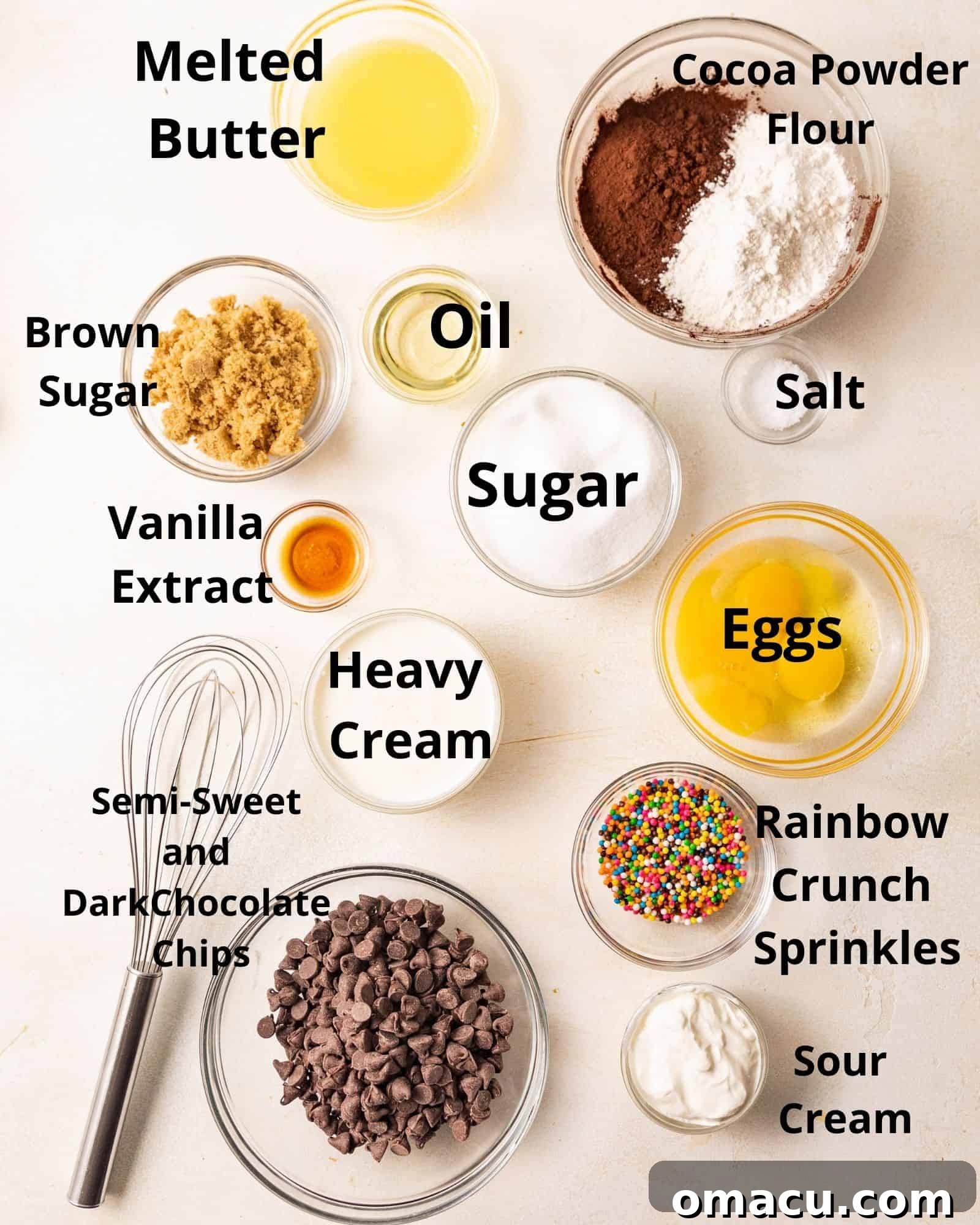Ingredients laid out for making cosmic brownies: melted butter, oil, brown sugar, white sugar, cocoa powder, flour, salt, eggs, vanilla extract, heavy cream, chocolate chips, sour cream, and rainbow crunch sprinkles.