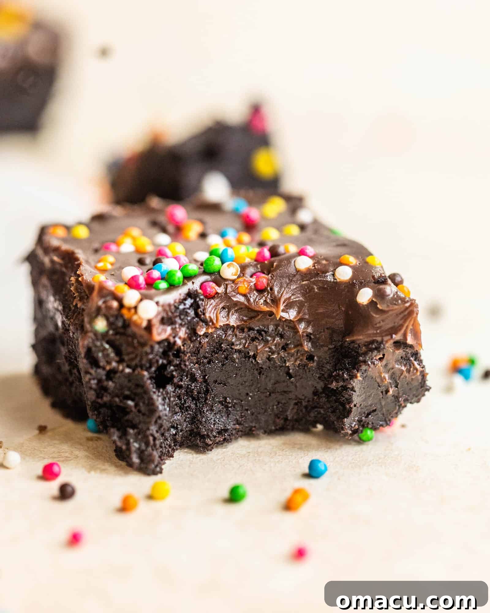 A single cosmic brownie with a bite taken out, showing the fudgy interior and thick ganache topping with sprinkles.