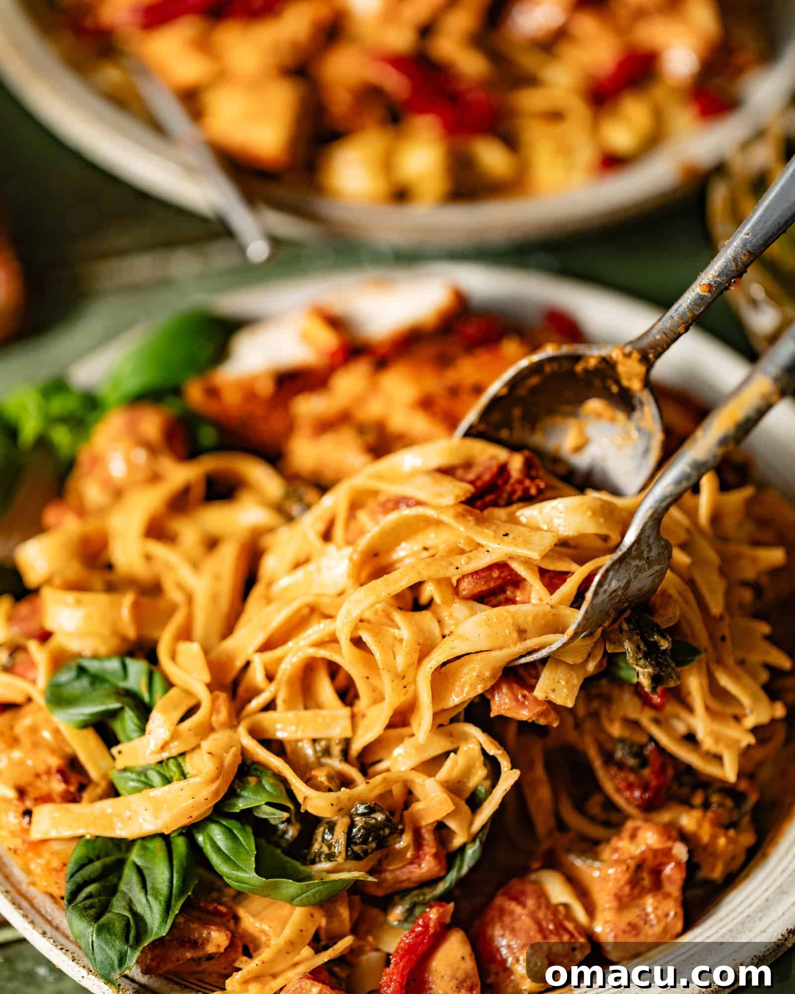 A fork and spoon elegantly twirling a generous portion of Marry Me Chicken Pasta off a pristine white plate, showcasing its creamy texture.