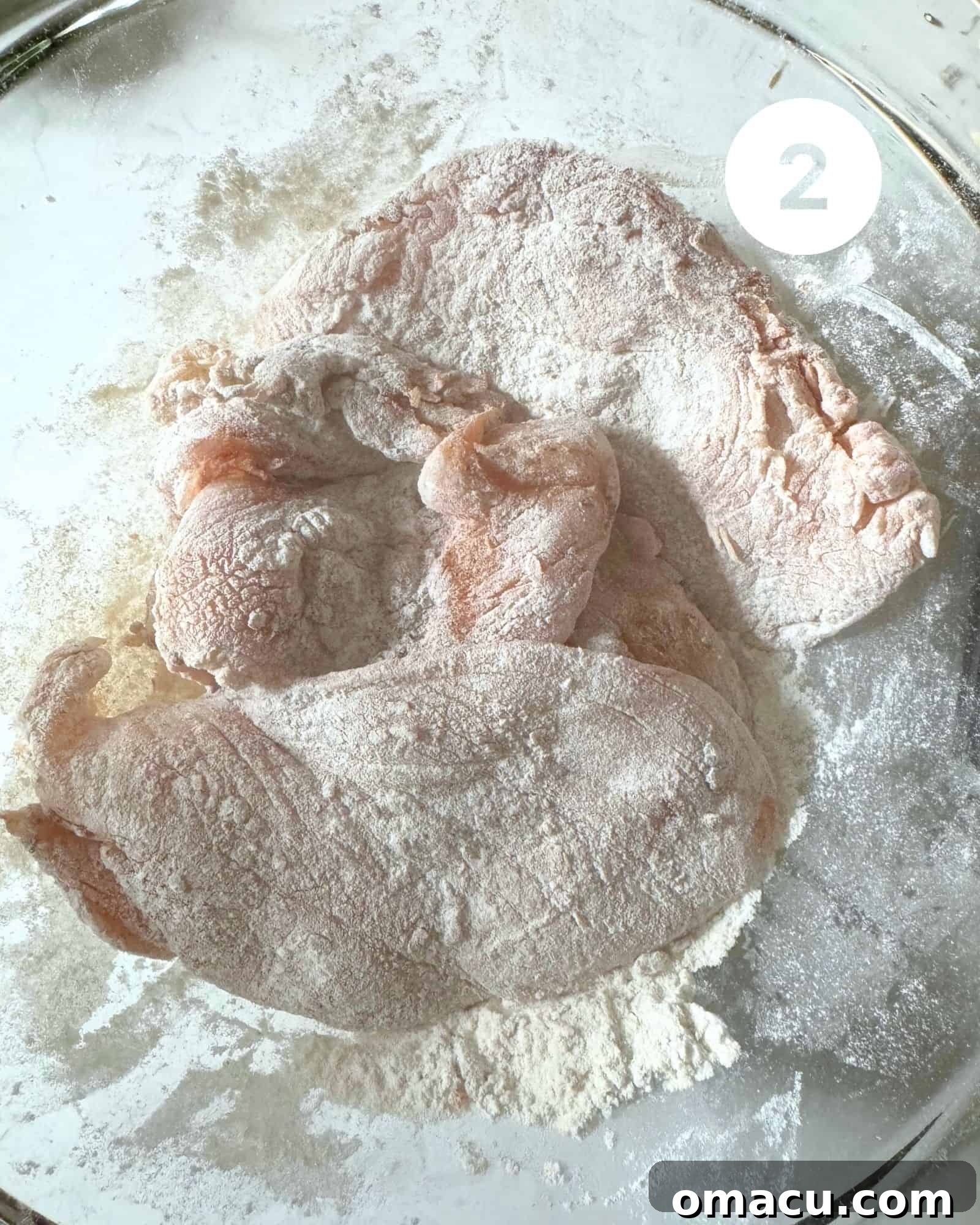 Pieces of chicken breast thoroughly coated in flour and various seasonings, resting in a mixing bowl, ready for sautéing.
