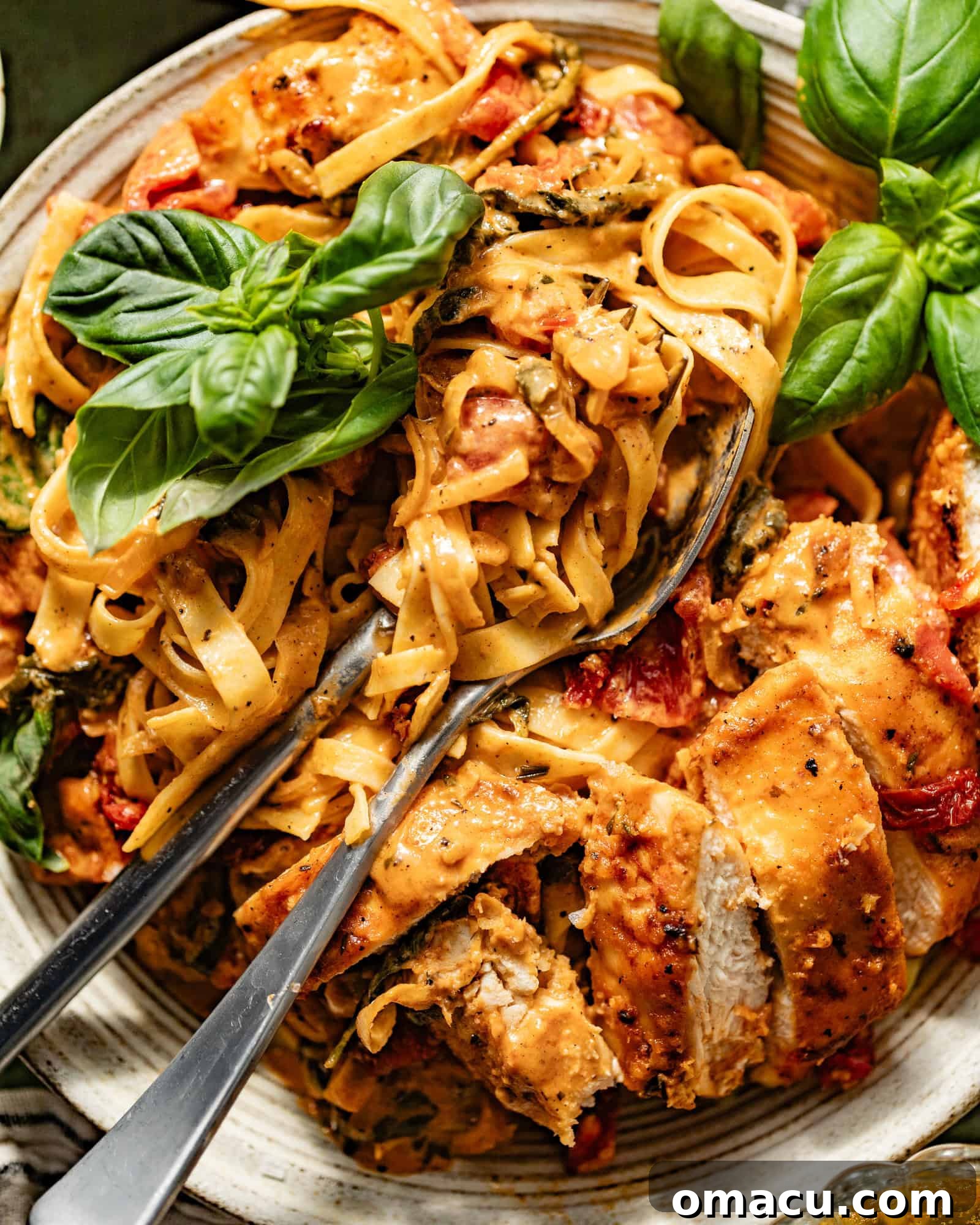 A close-up view of a fork and spoon lifting a generous, creamy bite of Marry Me Chicken Pasta from a plate, highlighting its texture.