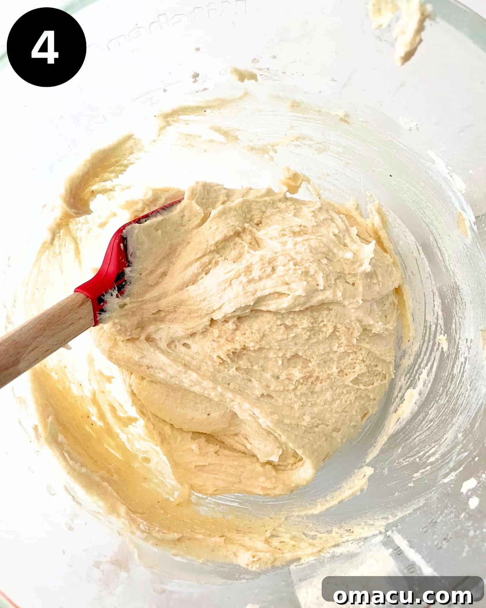 Smooth and well-mixed cake batter in a bowl, with a flat spatula demonstrating its soft consistency, ready for the next steps in baking.