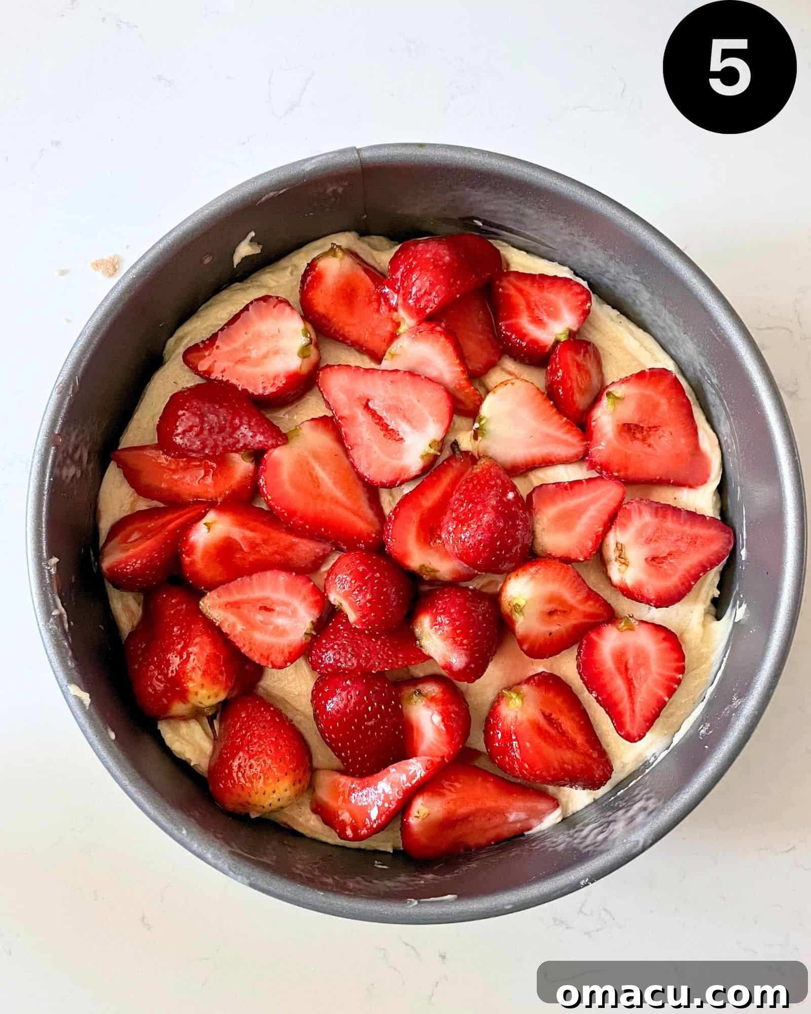 The delicate cake batter evenly spread in a springform pan, topped with a generous layer of vibrant sliced strawberries, ready for the crumb topping.