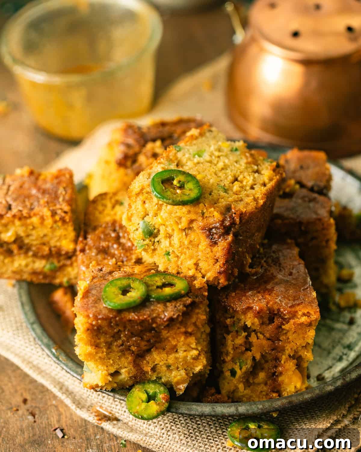 sliced pieces of jalapeno cornbread on a serving plate topped with fresh jalapenos and honey butter.