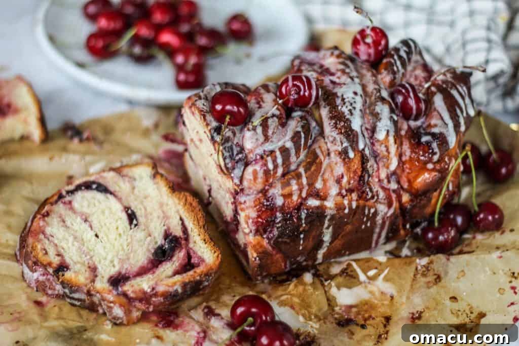 A freshly baked Cherry Cream Cheese Babka, swirled with red cherry filling and creamy white cream cheese, on a cooling rack.
