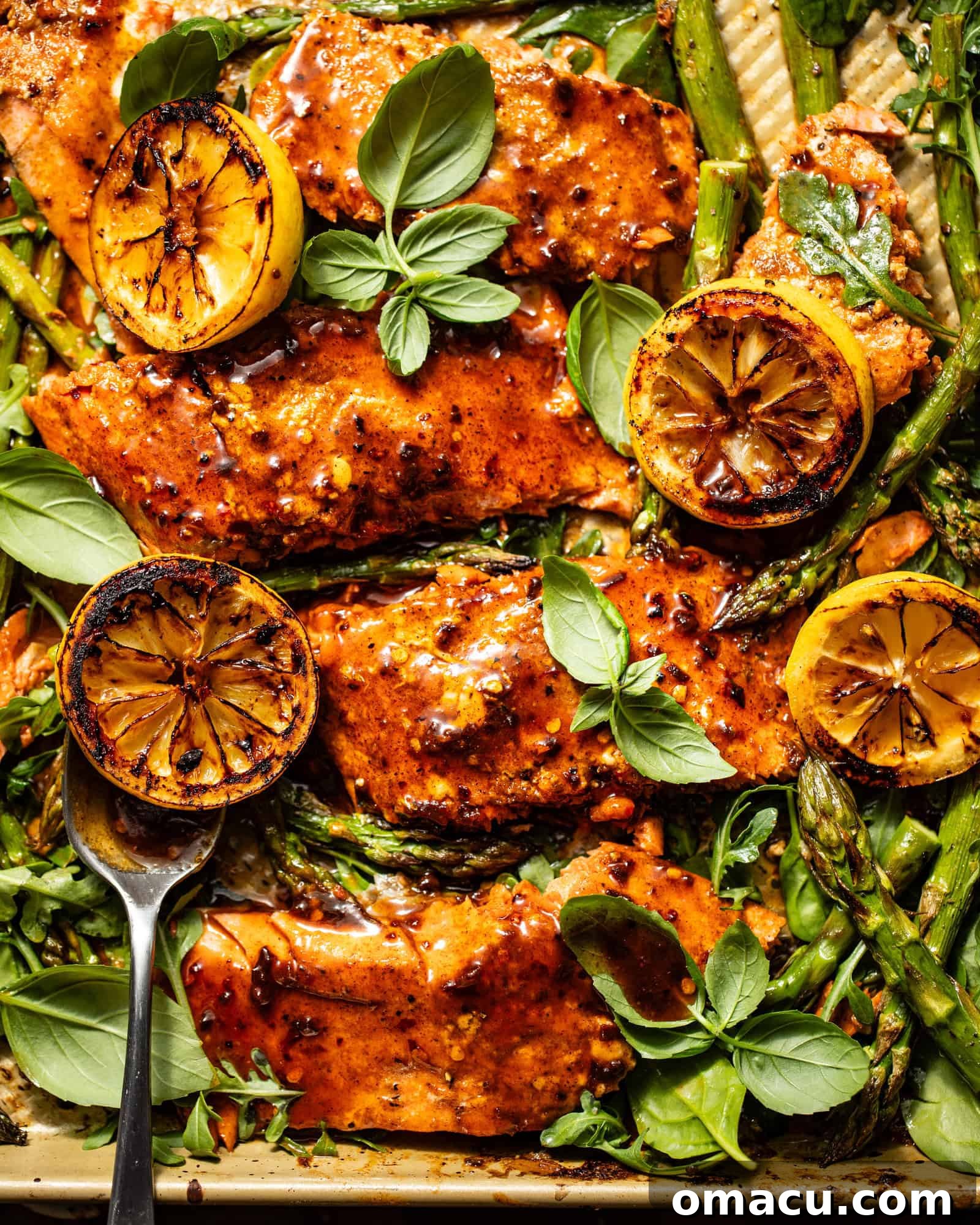 Cajun Honey Butter Salmon on a sheet pan with roasted asparagus, charred lemons, and fresh arugula for garnish.