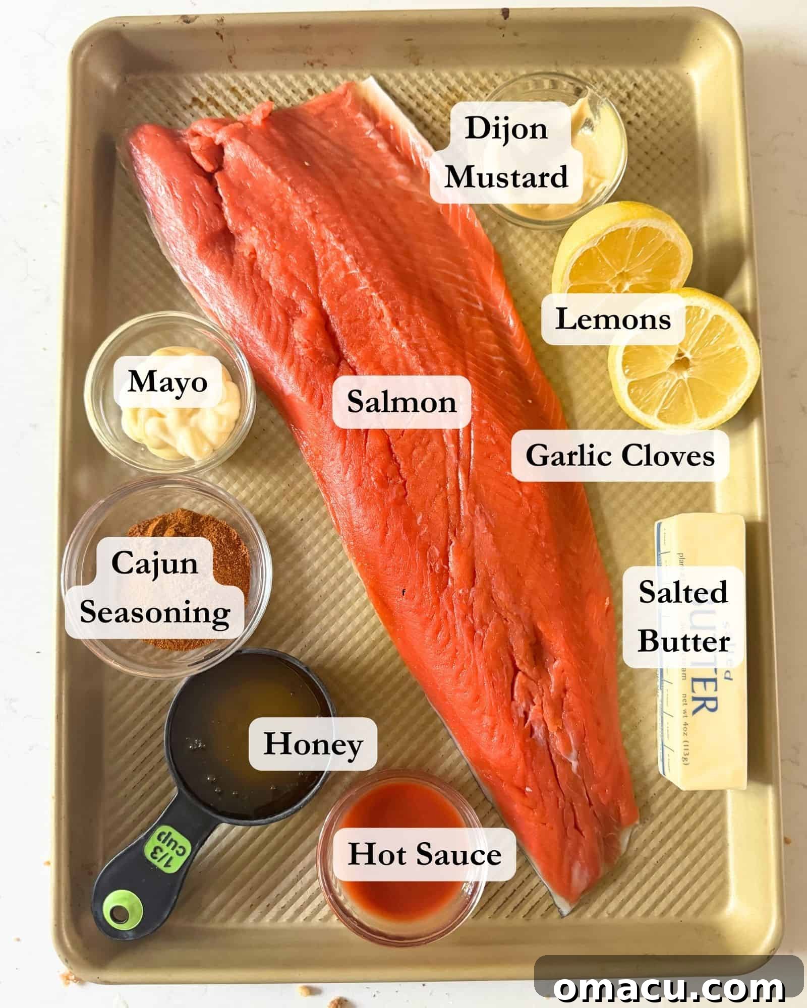 Ingredients for making Cajun Honey Butter Salmon laid out on a sheet pan, including salmon fillets, asparagus, and various spices and sauces.