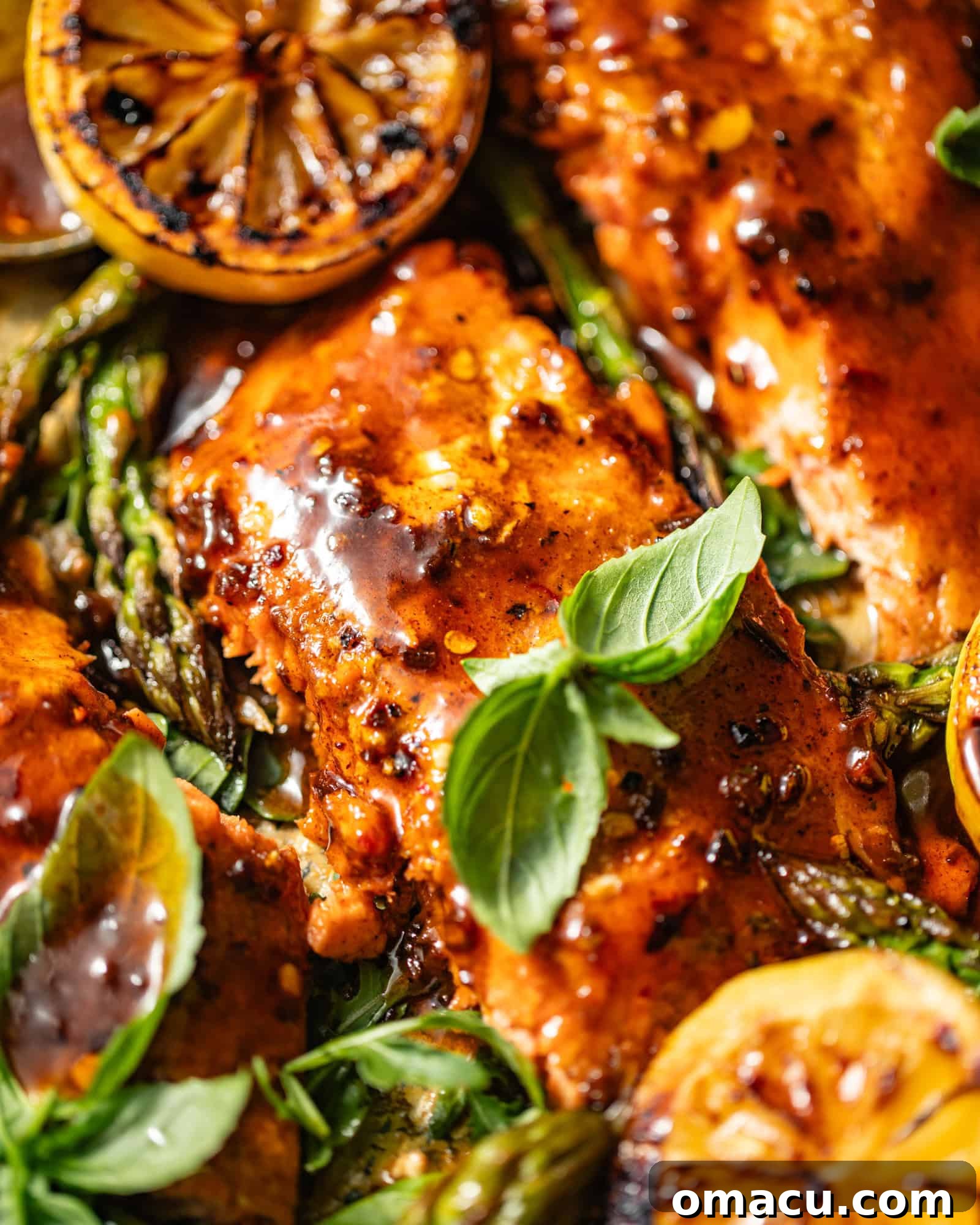 Up close view of glazed Cajun Honey Butter Salmon on a sheet pan, garnished with fresh basil leaves, showcasing its crispy skin and vibrant sauce.